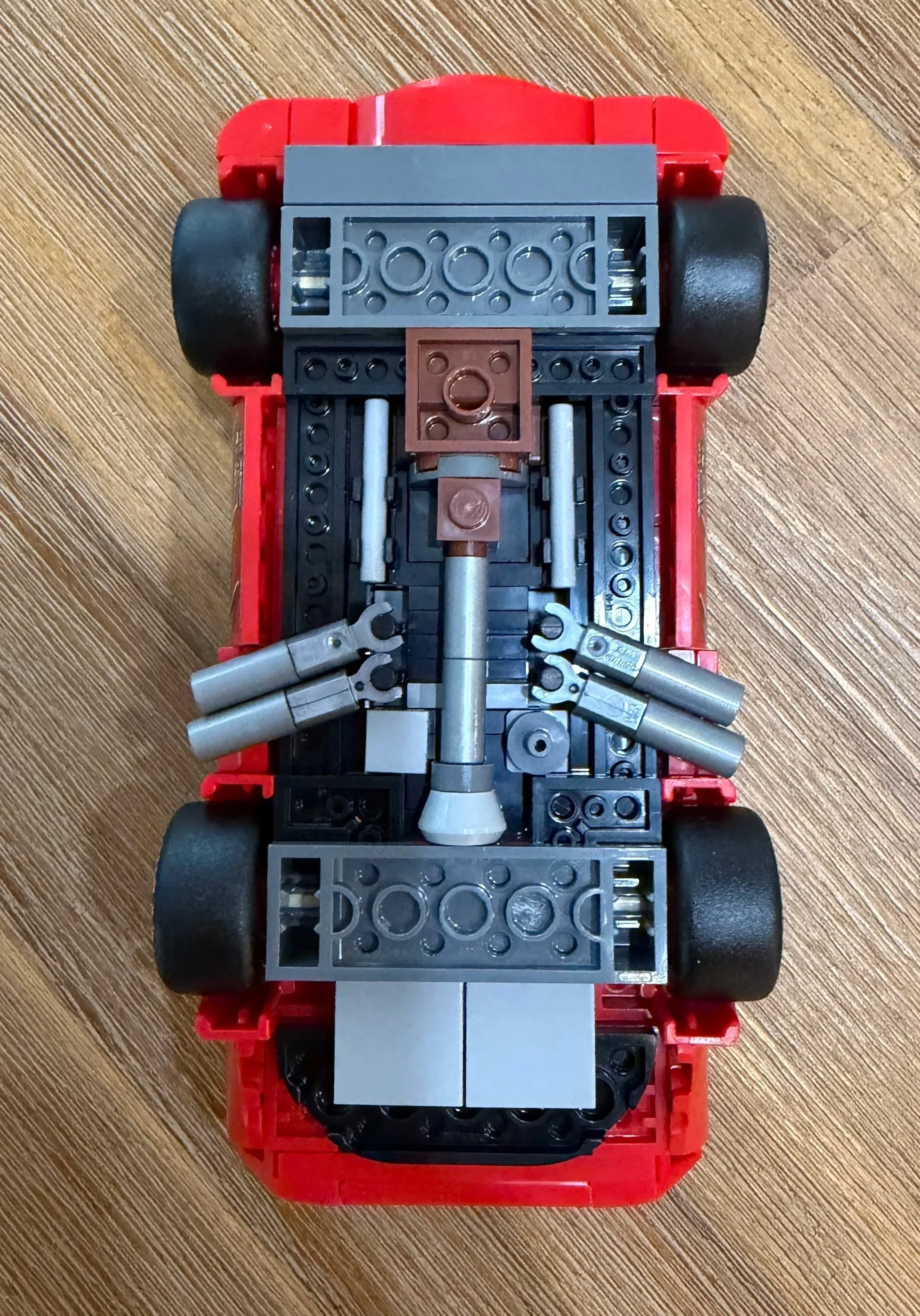 Underside of LEGO Lightning McQueen showing four tires, gray undercarriage details, and paired silver exhaust outlets on both sides.