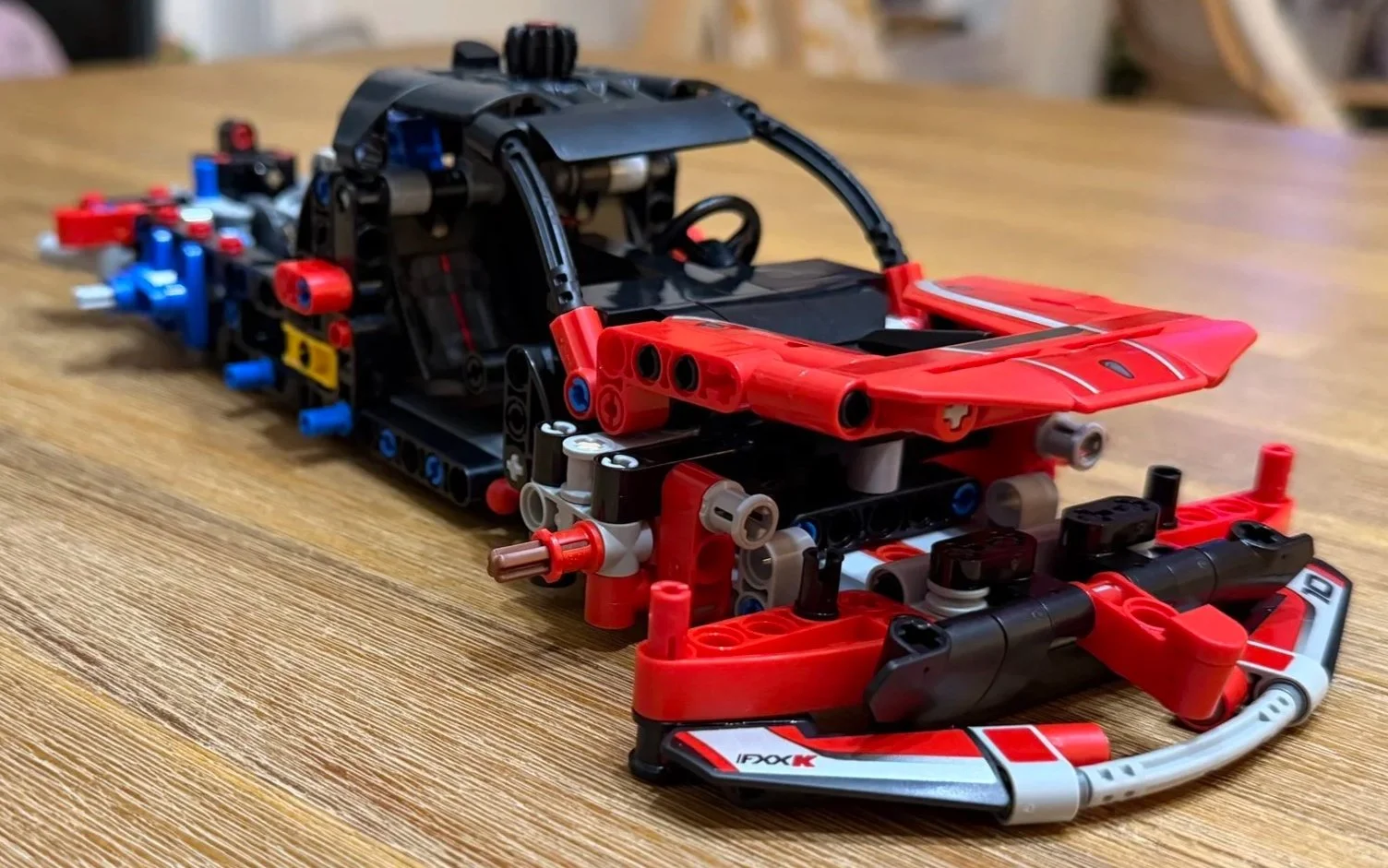 Partly built Ferrari FXX K with a raised red front hood, curved gray lower bumper, black windshield frame, and roof steering gear.