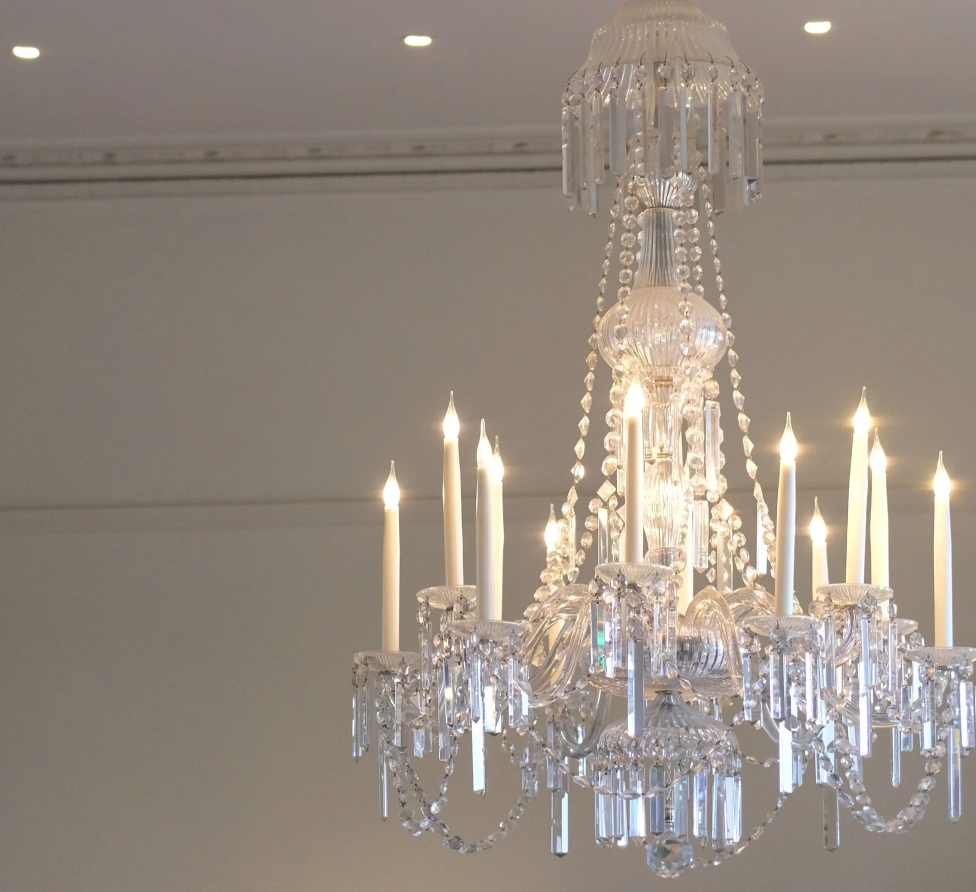 Elegant crystal chandelier with lit white candles hanging from a white ceiling at a wedding in Edmonton, Alberta, Canada.