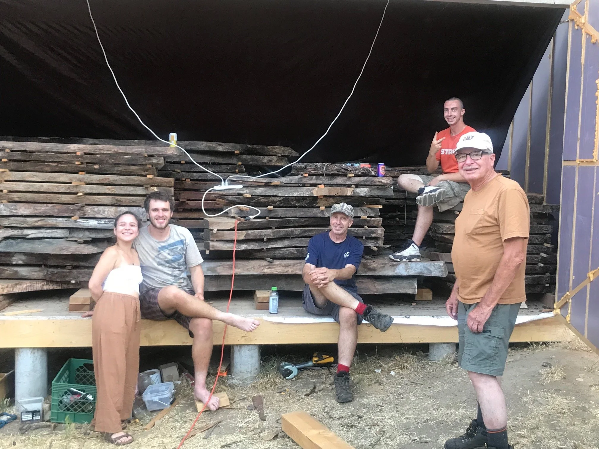 Group of five people smiling and posing in front of wooden stacks during a construction project, with tools and supplies around them.