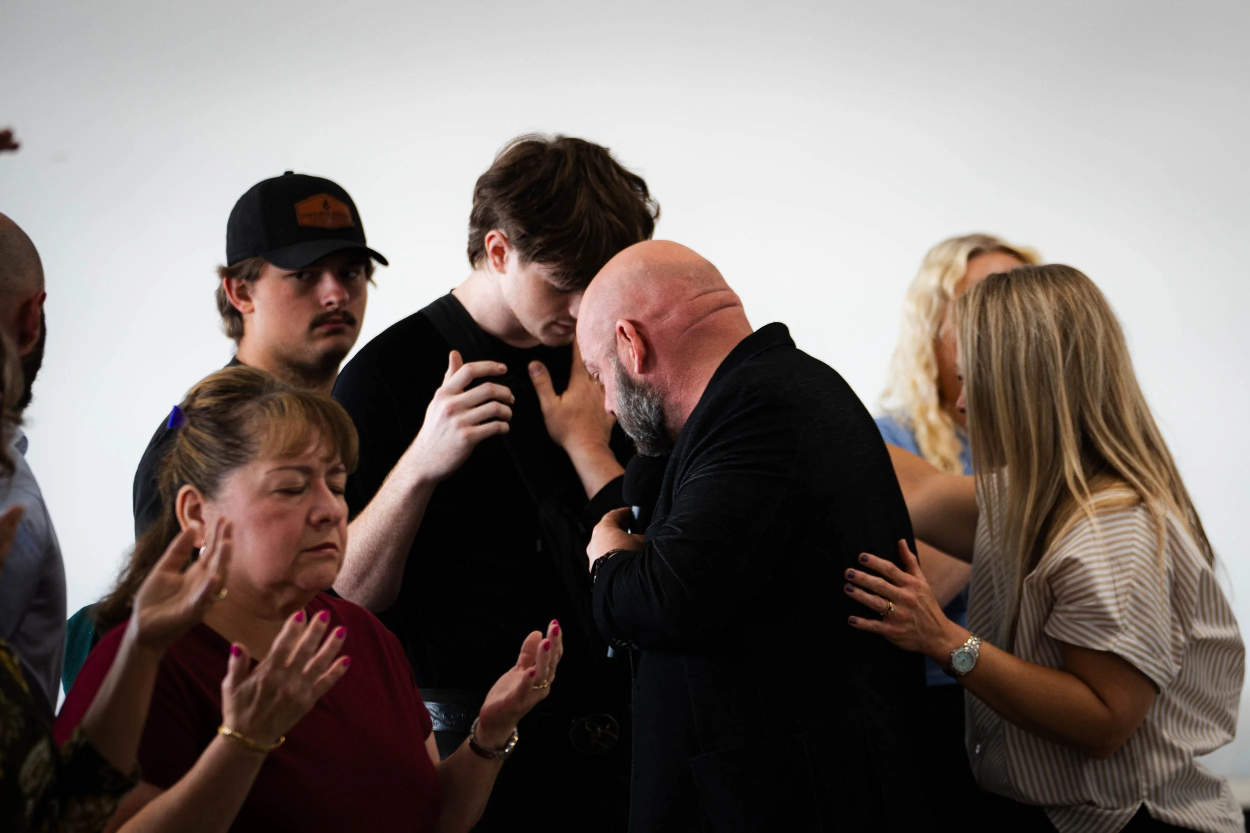 Group of people praying and comforting each other with eyes closed and hands raised.