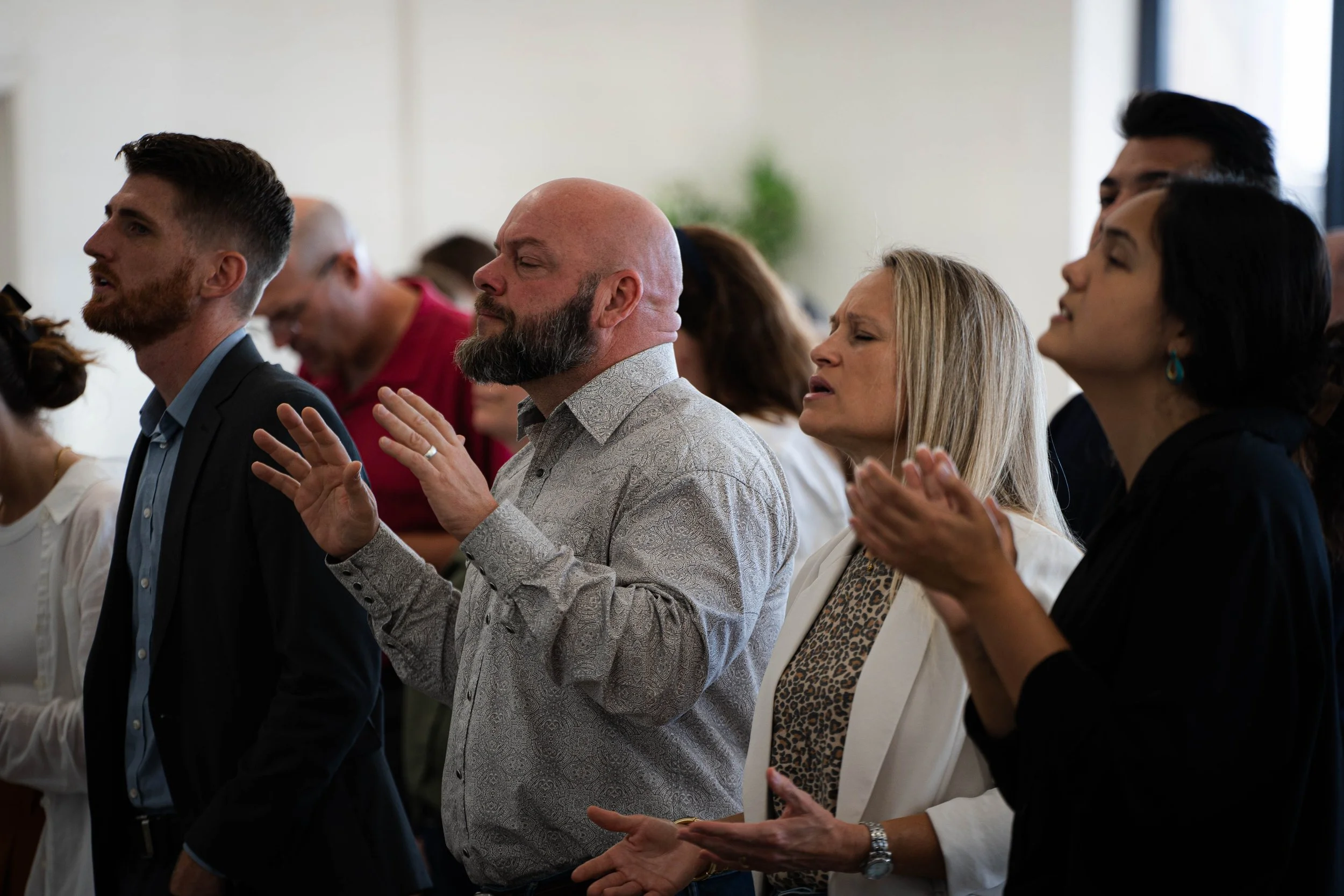 People praying and worshiping with eyes closed and hands raised during a church service or gathering.