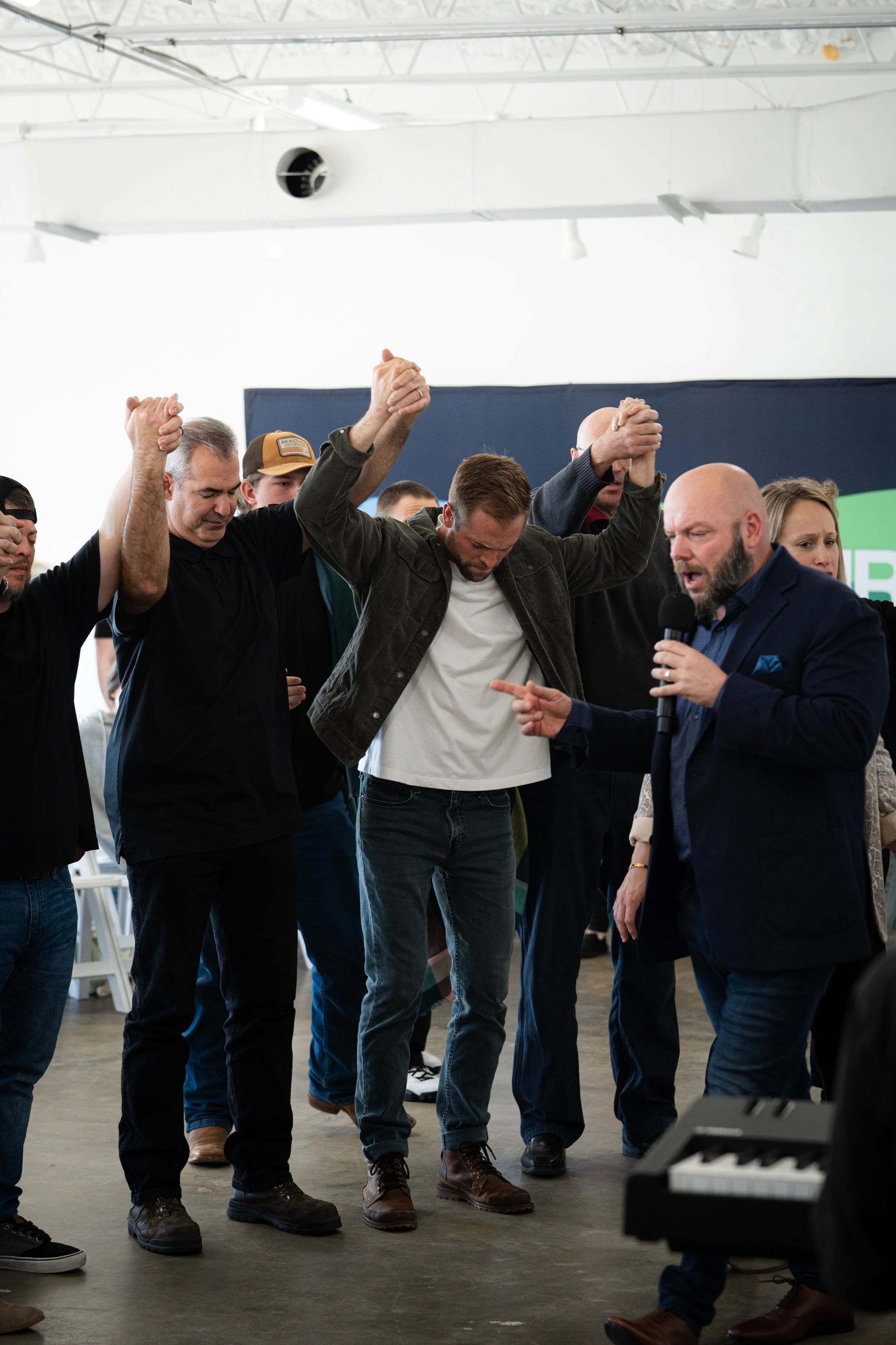 A group of people holding hands and praying while a man speaks into a microphone.