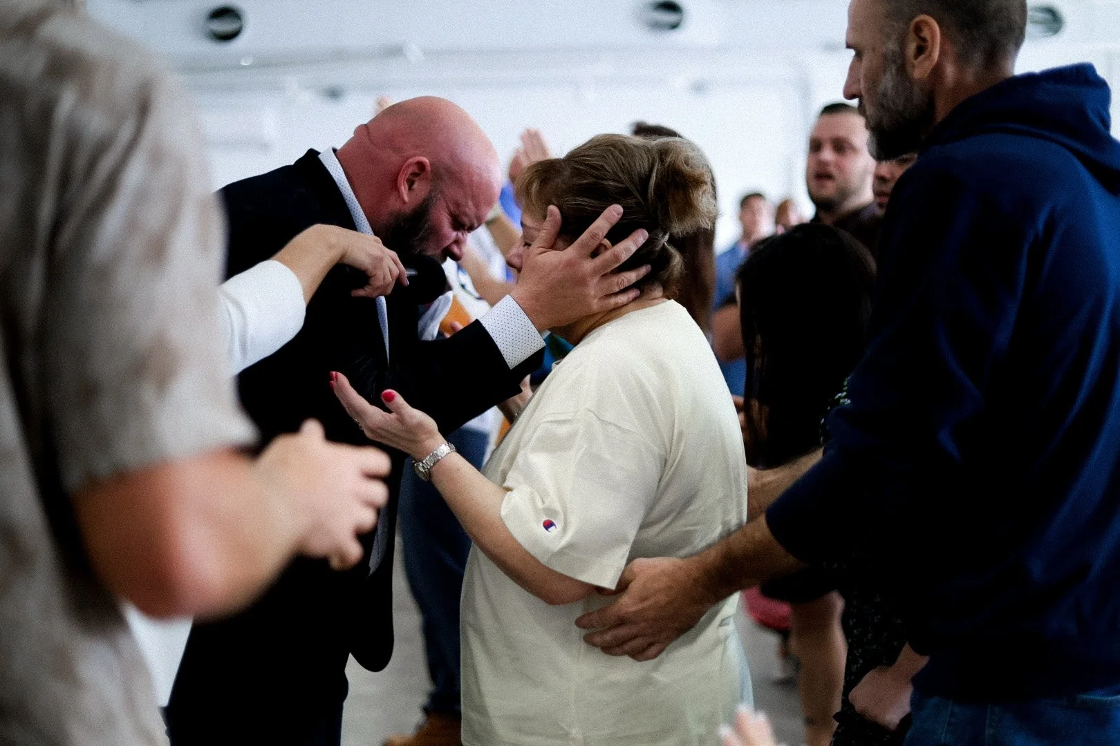 A woman is crying while being comforted by a man with his hands on her shoulders and a woman touching her hair, in a crowded indoor setting.