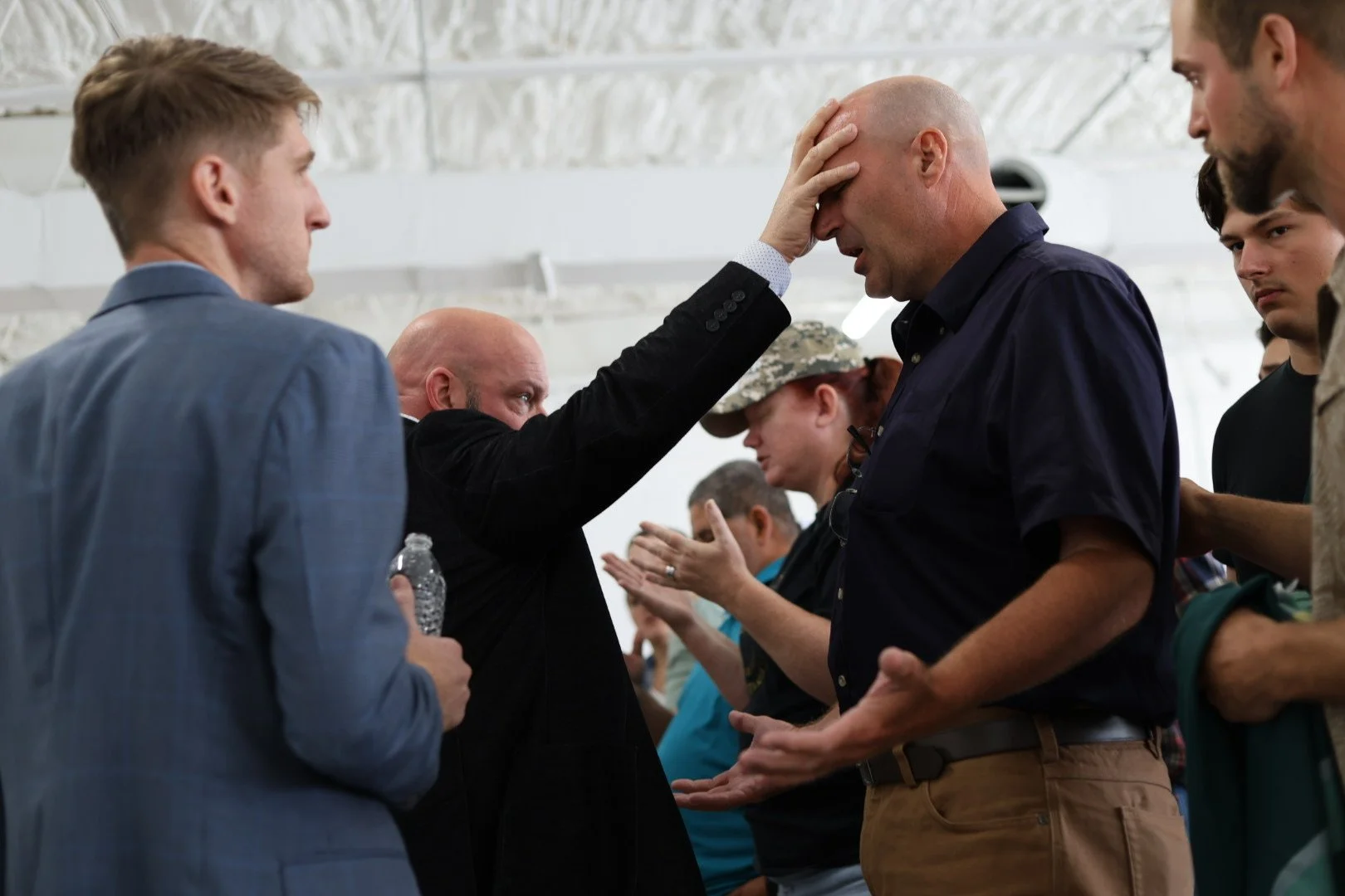 People praying in a group, with a man in black touching another man's forehead