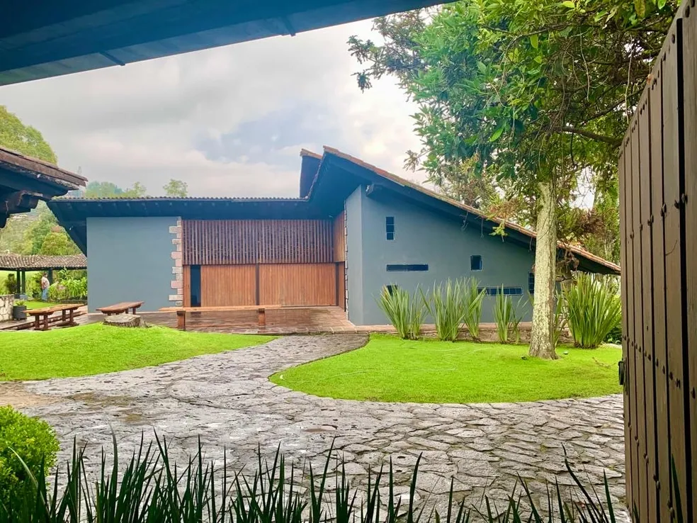 Vista de una casa moderna con un jardín verde y caminos de piedra, rodeada de árboles y vegetación
