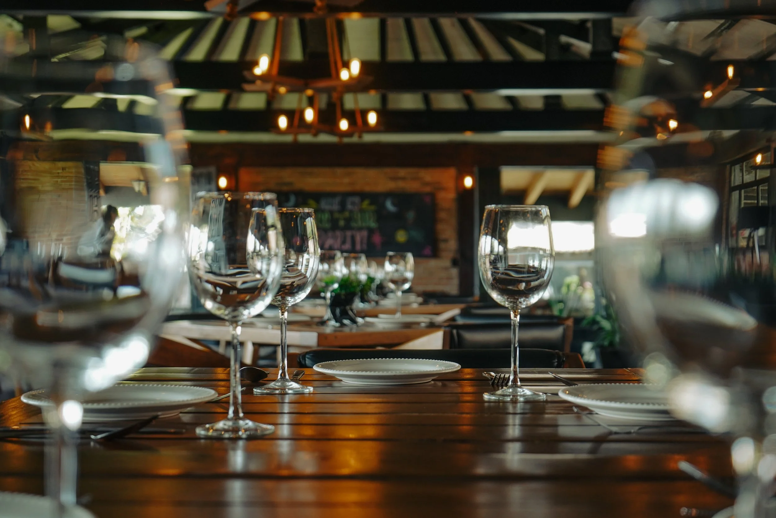 Mesa de restaurante con copas de vino, platos y cubiertos en un ambiente acogedor con iluminación cálida y decoración rústica.