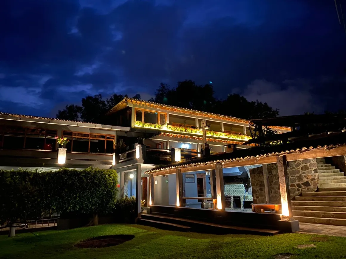 Edificio con iluminación exterior y cielo nocturno, rodeado de vegetación y escaleras de piedra.