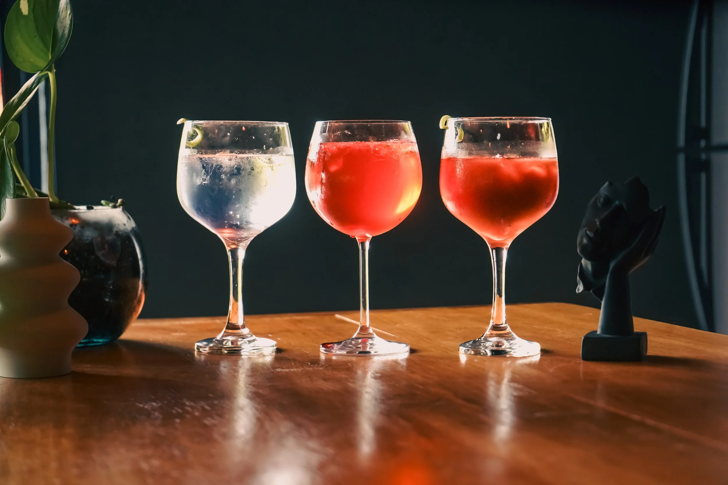 Tres copas de cóctel con líquidos de diferentes colores, decoradas con rodajas de limón, sobre una mesa de madera.