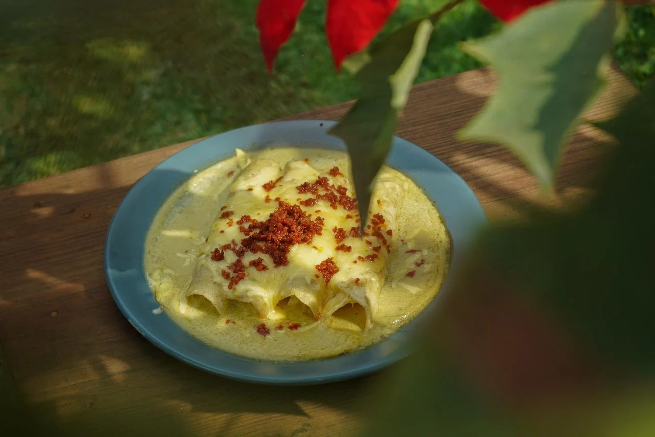 Plato de enchiladas con salsa verde, queso y carne picada, adornado con un toque de crema y acompañado de hojas de poinsettia decorativas.