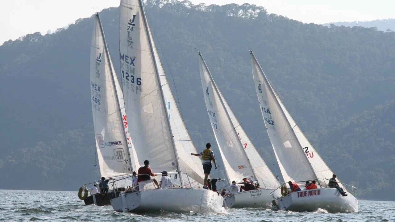 Tres barcos de vela compitiendo en el agua con una montaña de fondo.