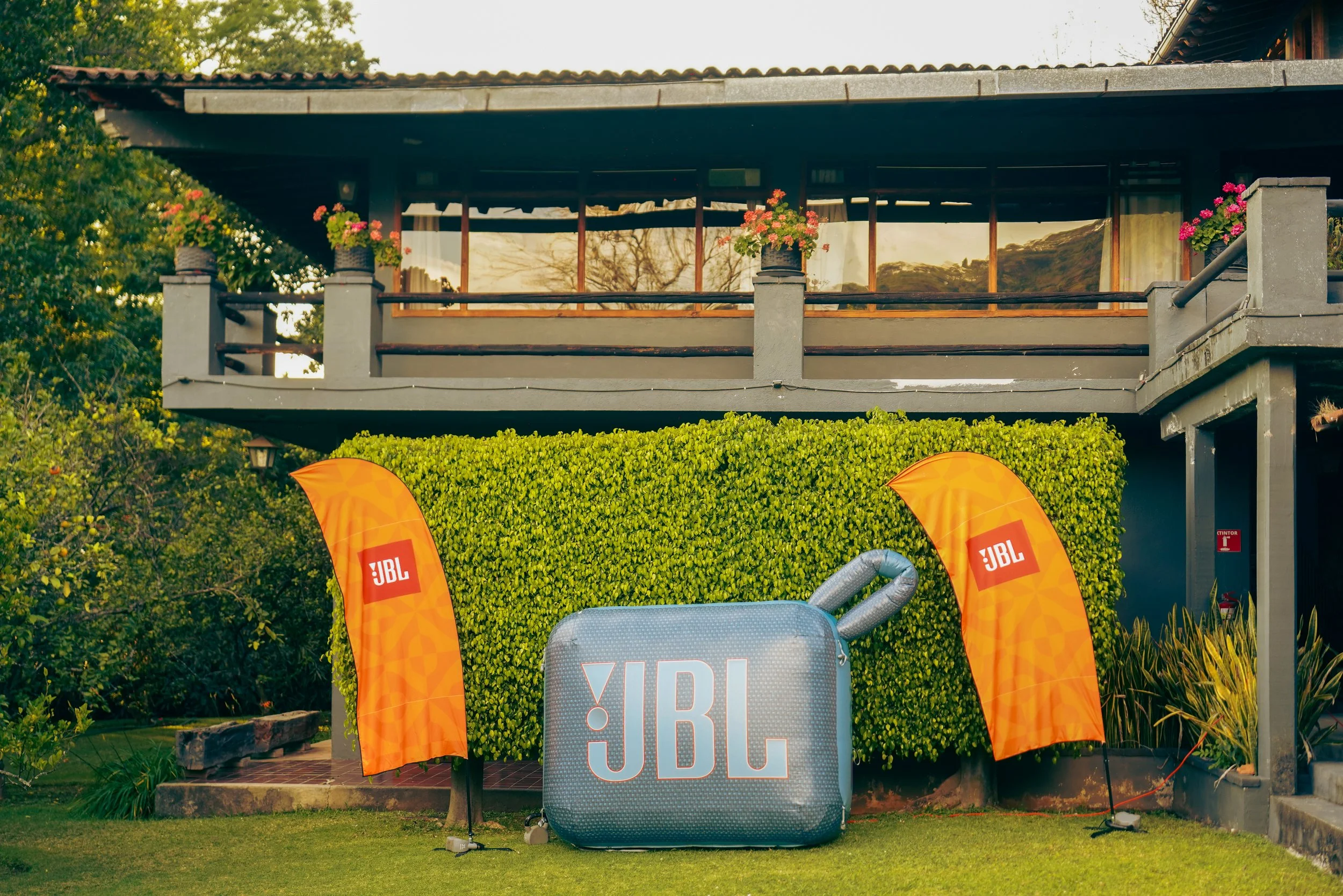 Decoración exterior con banderas y altavoz de la marca JBL frente a una casa con balcón y vegetación.