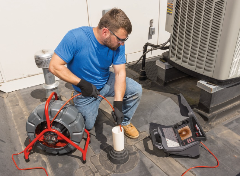 Technician inspecting a drain pipe with a camera inspection device in a commercial or industrial setting.
