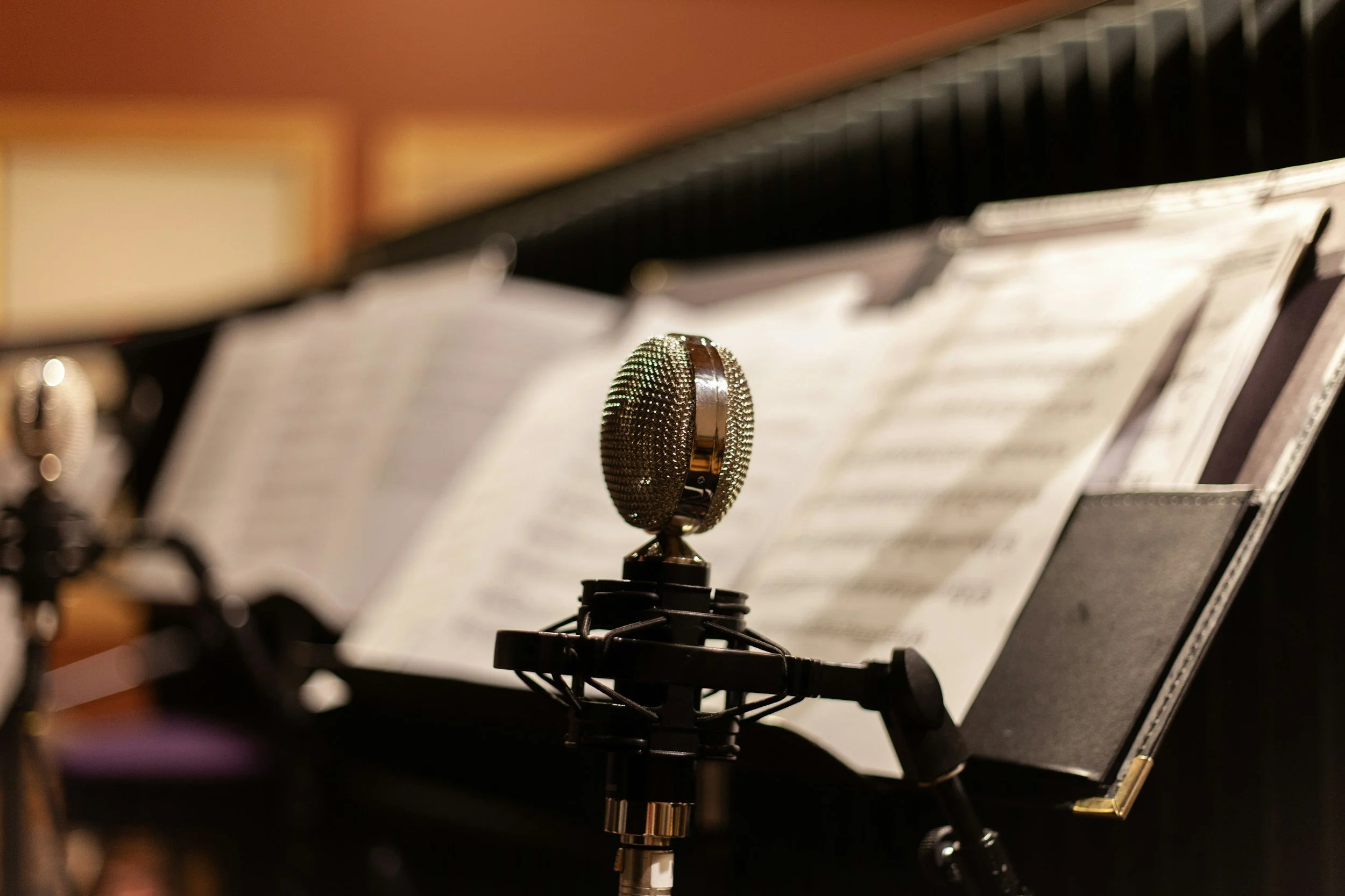 Close-up of a vintage microphone on a stand in front of music sheets on a music stand.