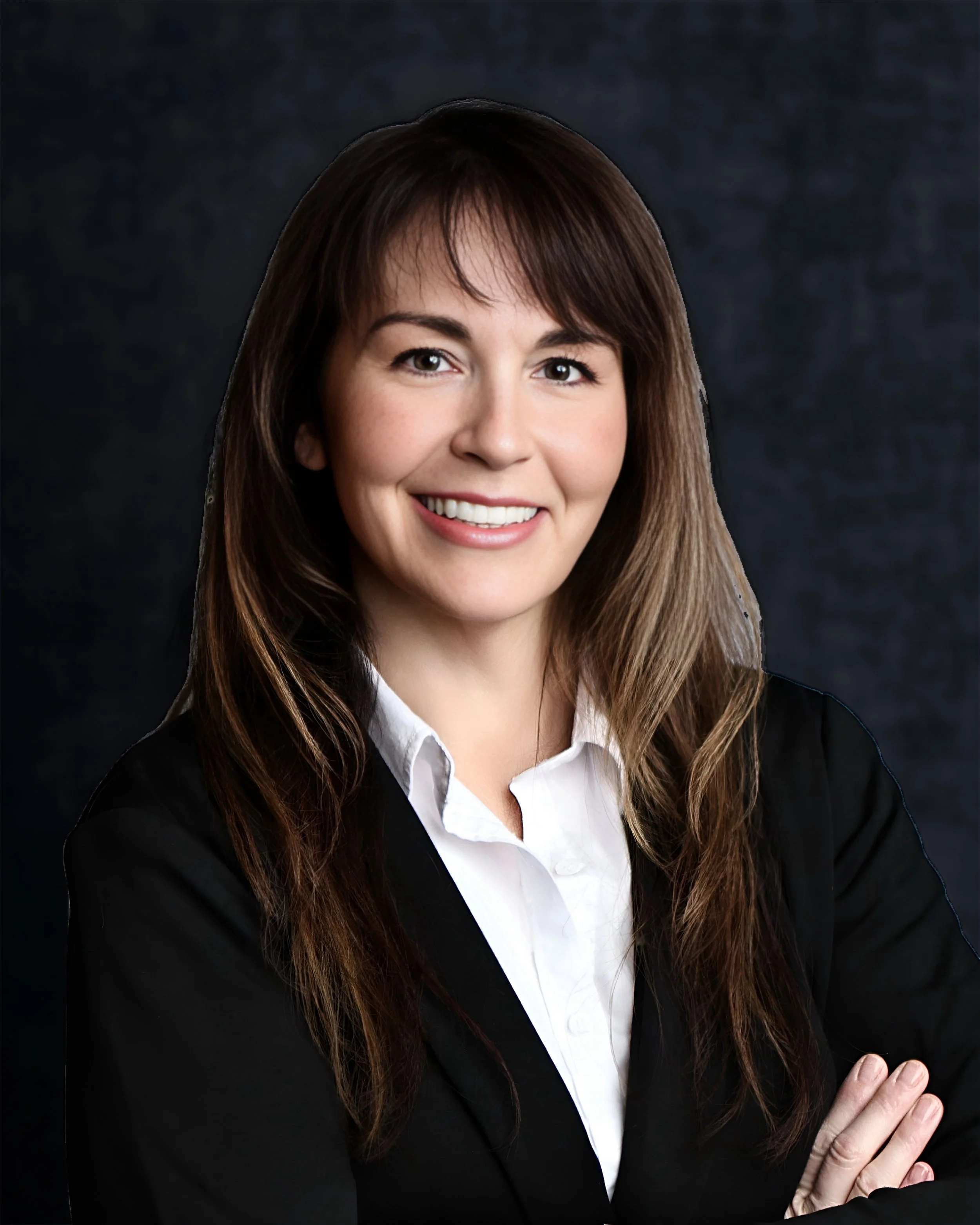 Professional headshot of a woman with long brown hair, wearing a black blazer and white shirt, smiling with arms crossed against a dark background.