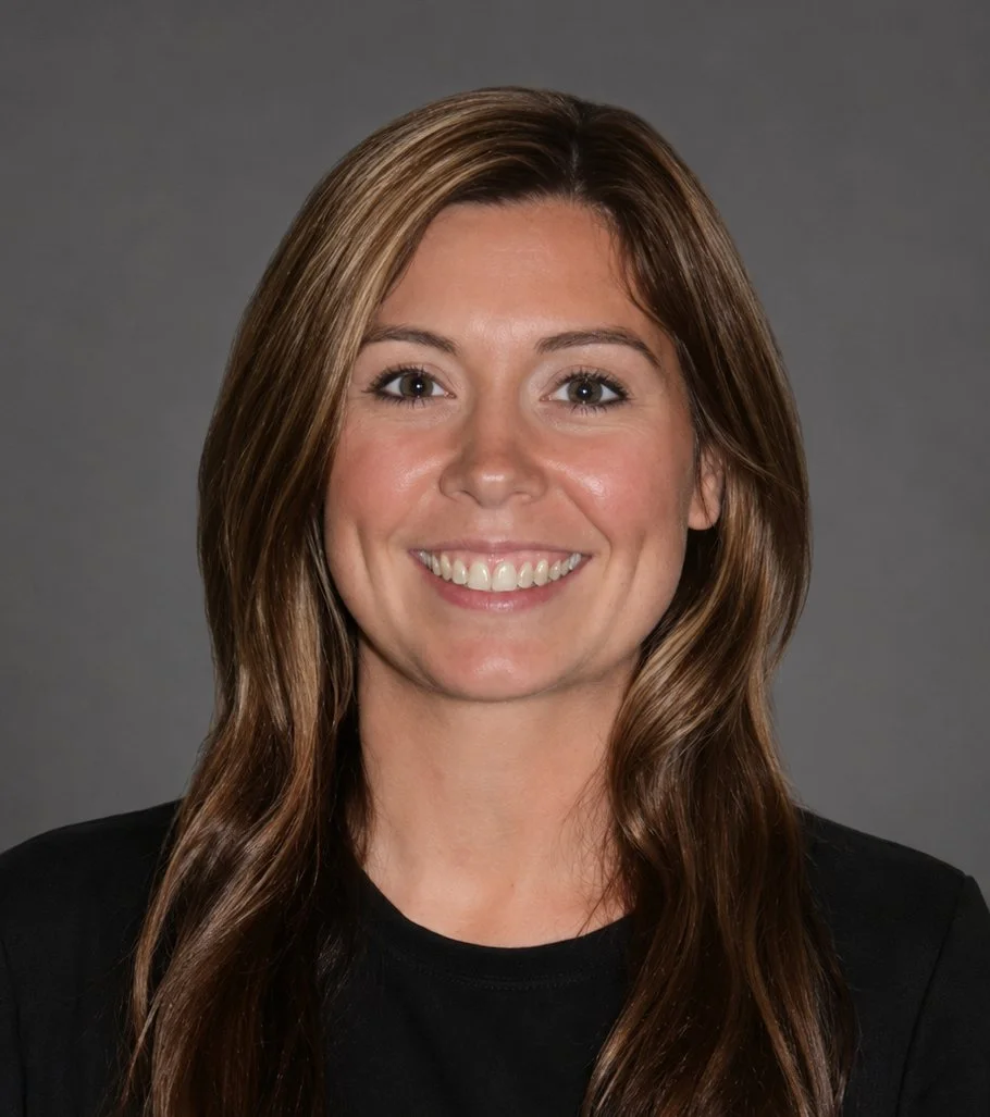 A young woman with long wavy brown hair, smiling showing her teeth, wearing a black top against a dark background.
