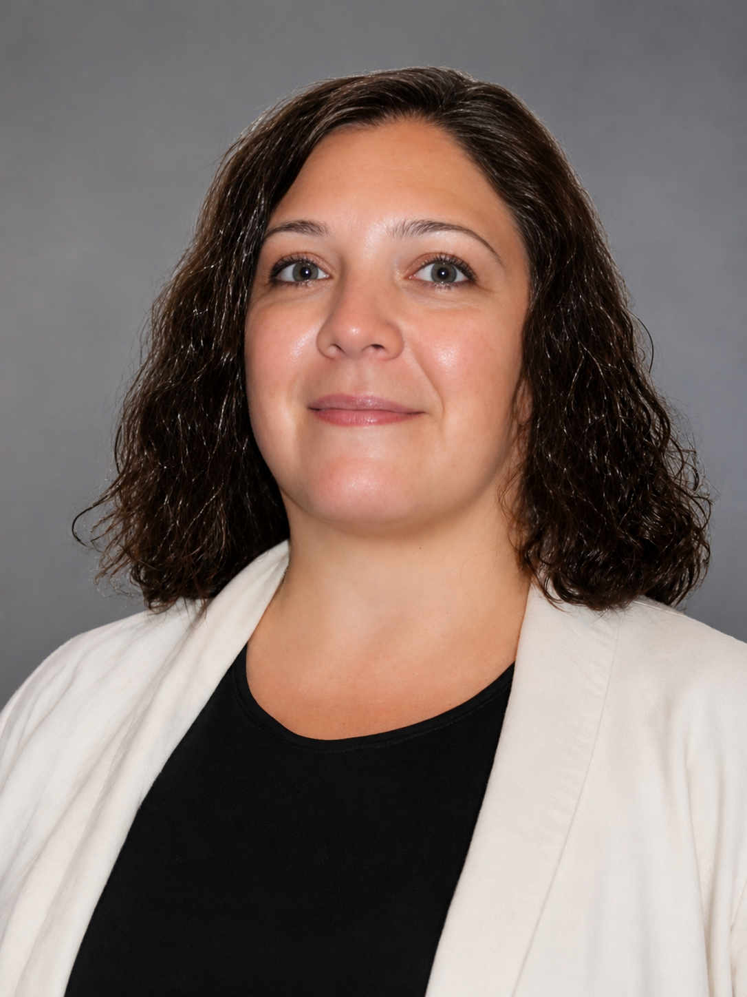 Image of a woman with shoulder-length dark brown hair, blue eyes, wearing a black top and cream blazer, against a black background.