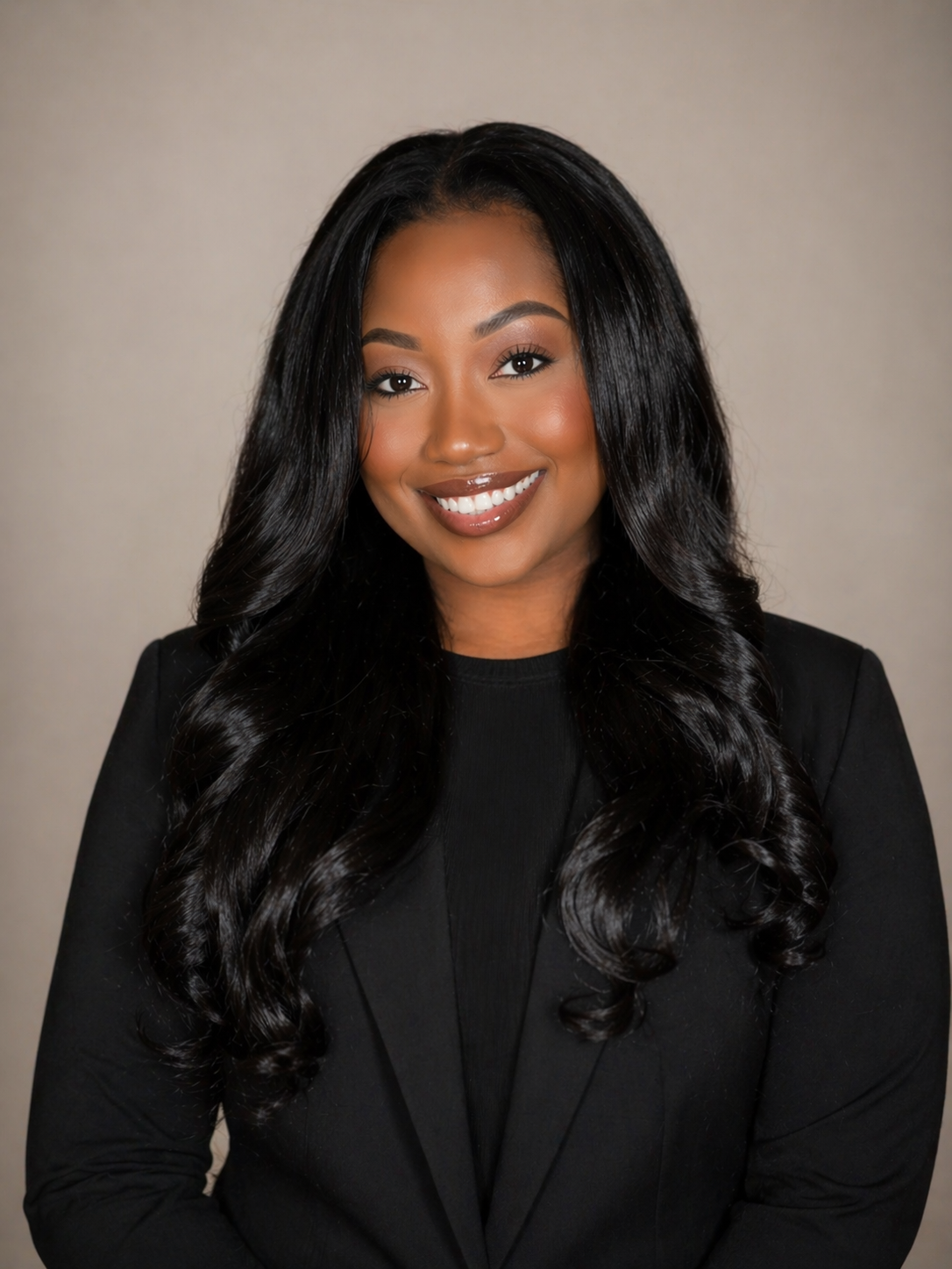 Headshot of a smiling woman with long, wavy black hair wearing a black blazer and top.