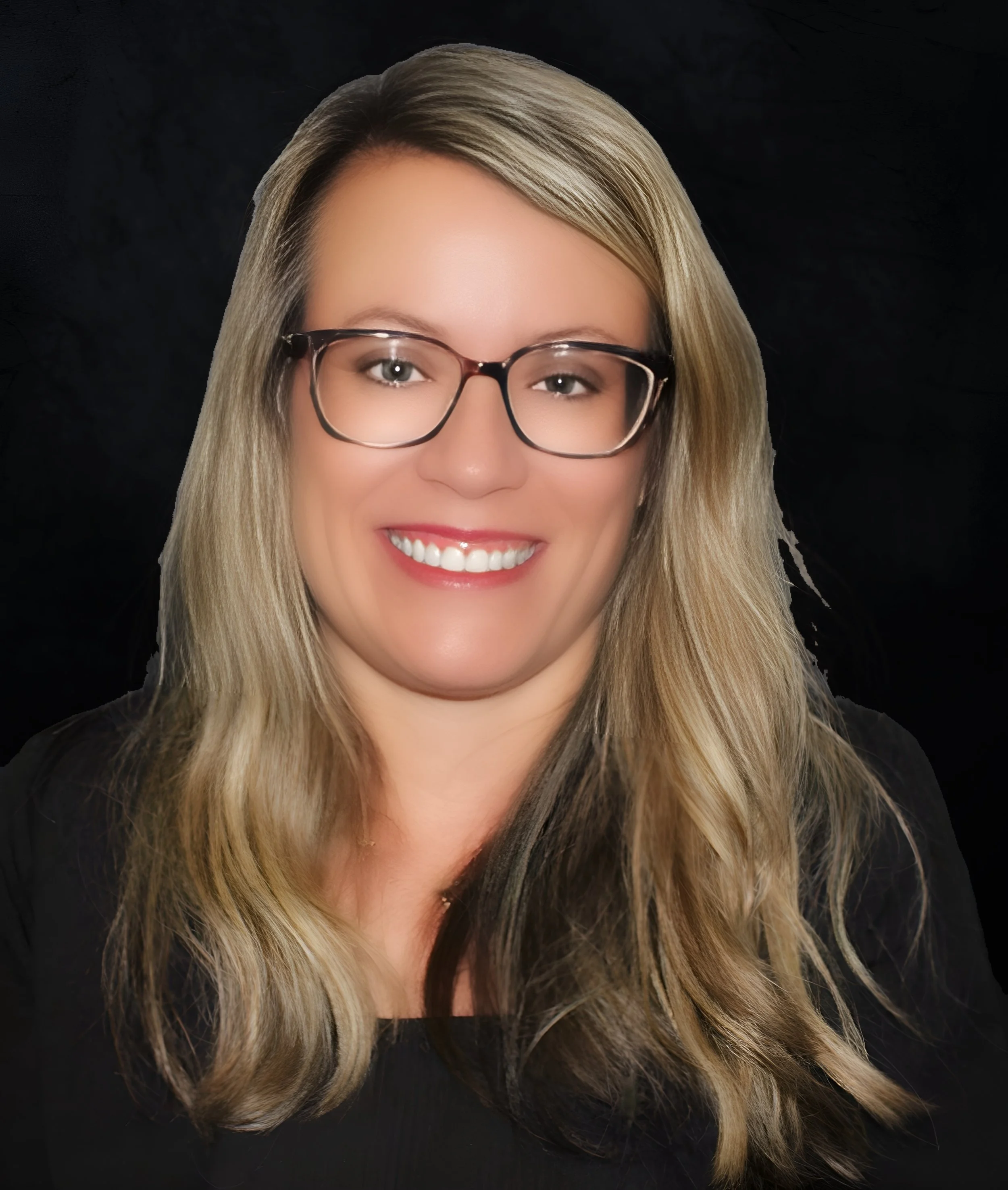A woman with long blonde hair, glasses, and a black top smiling against a black background.