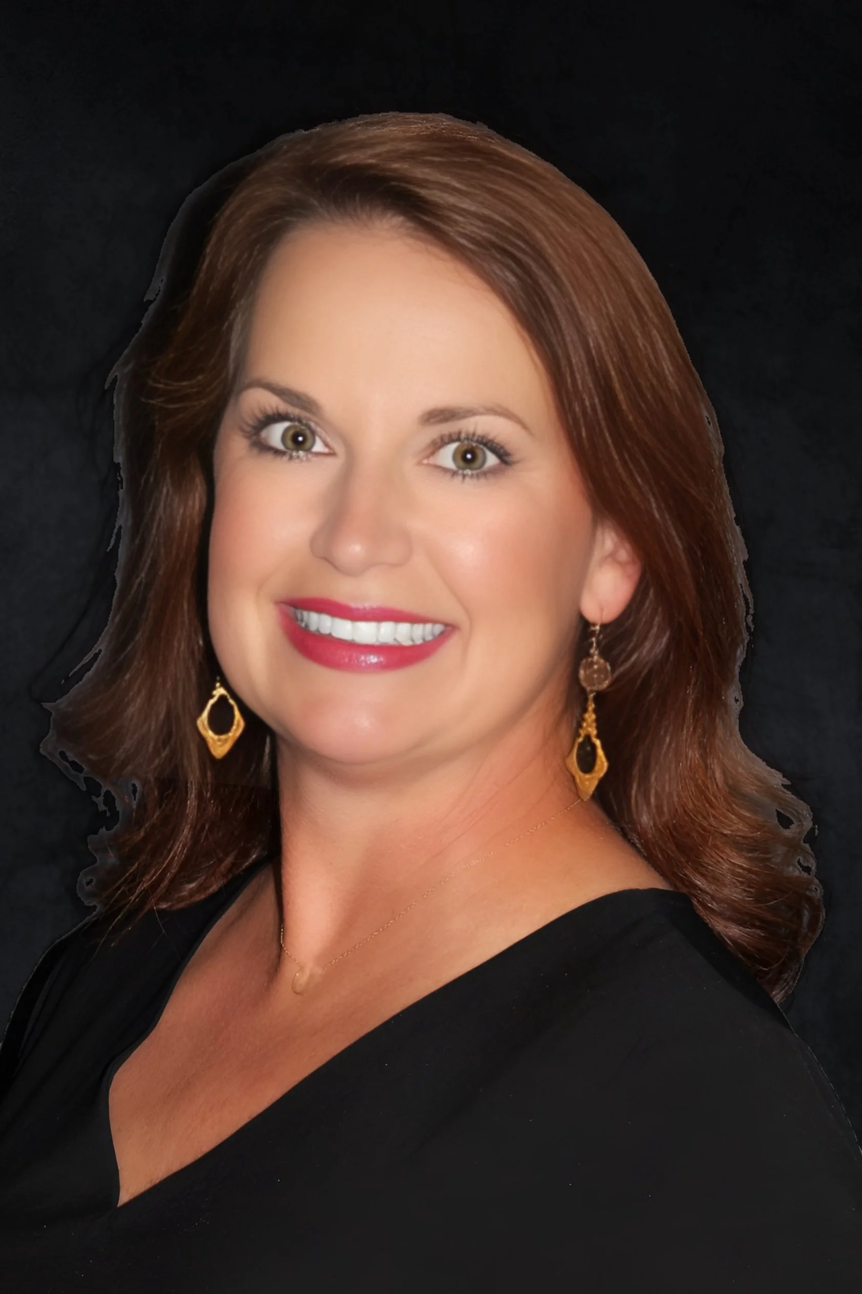 A woman with shoulder-length brown hair smiling in front of a black background, wearing gold earrings and a black top.