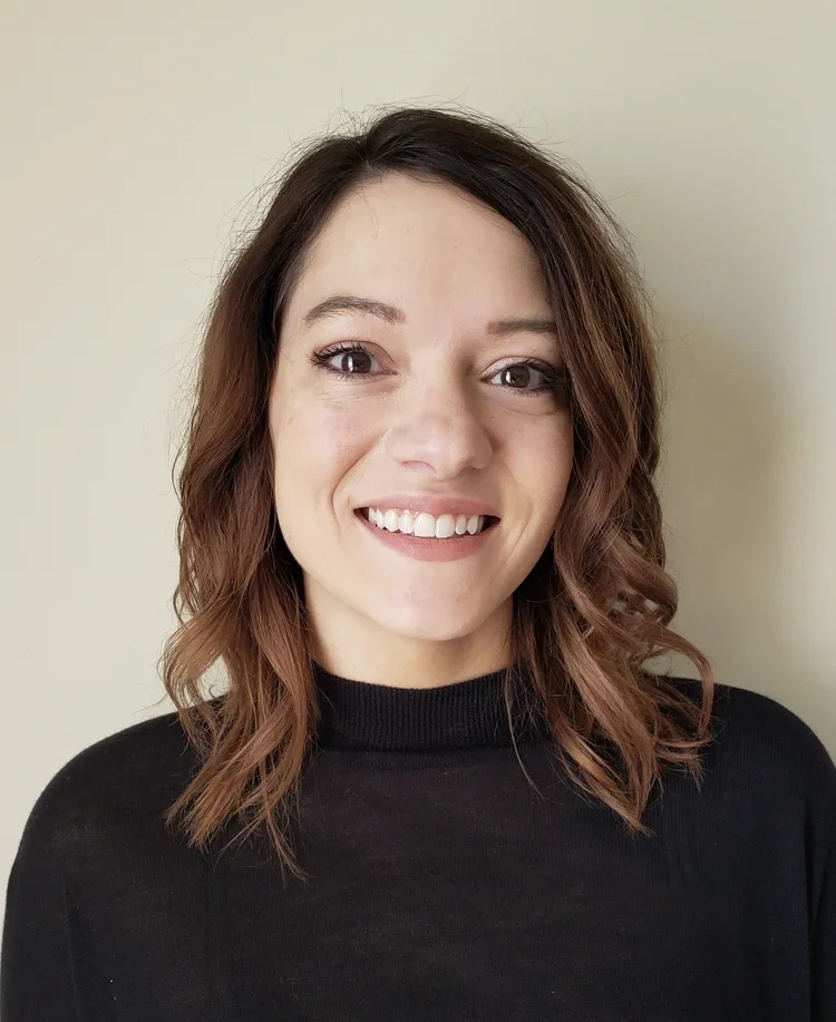 Headshot of a smiling woman with brown hair wearing a black top.