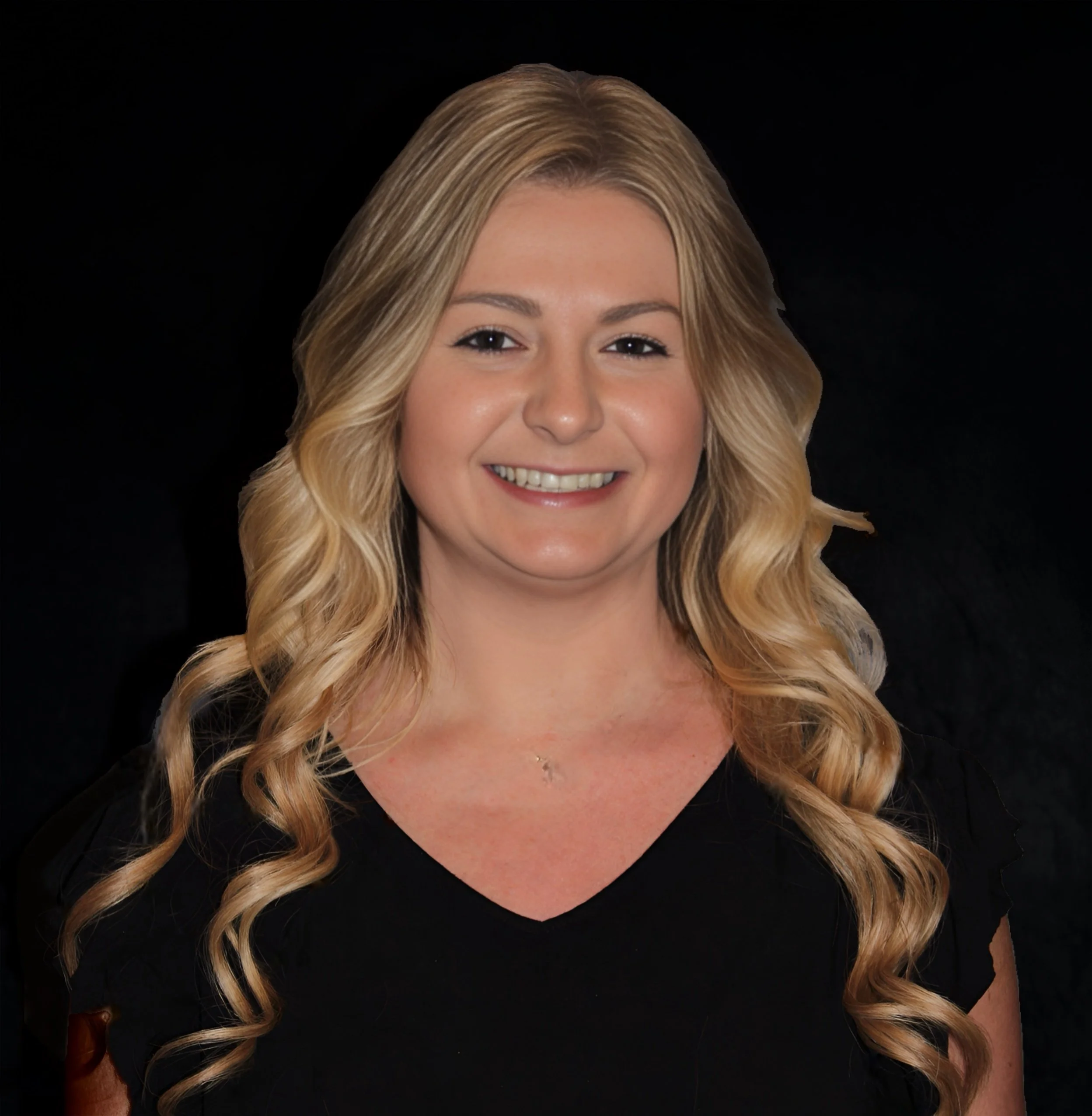 A woman with blonde, wavy hair, smiling, wearing a black top with a V-neck, against a black background.