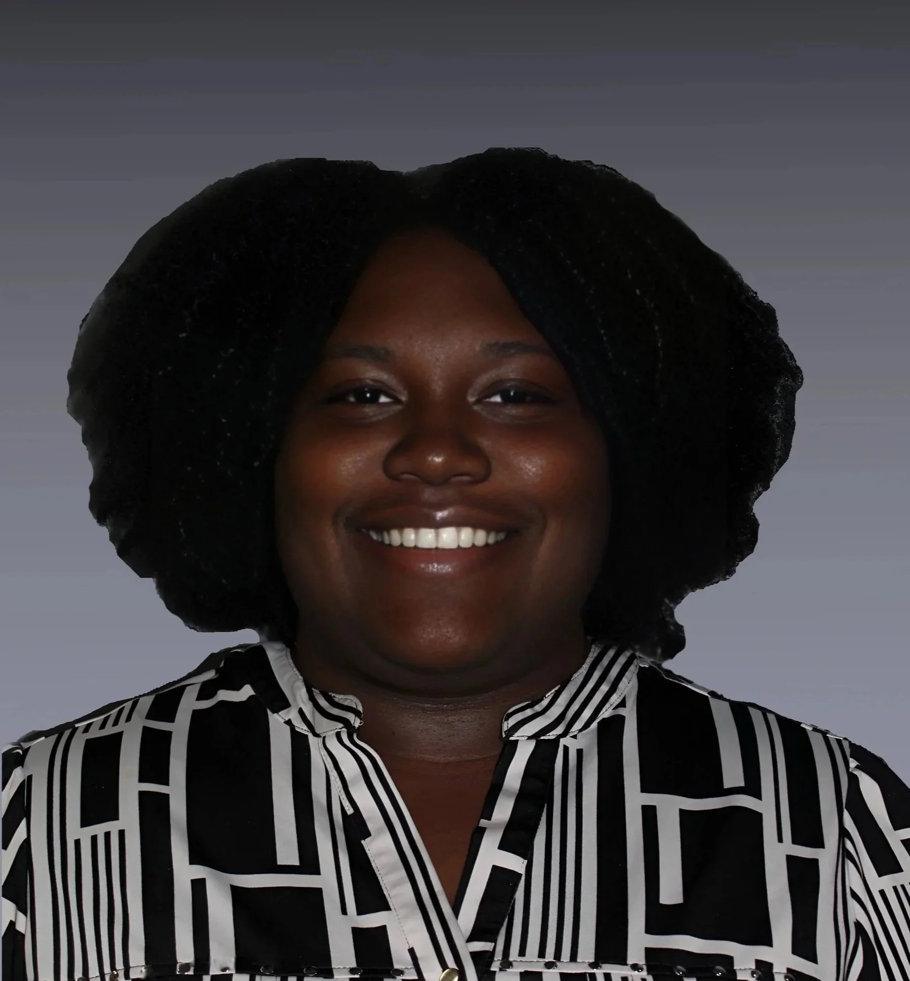 A woman with dark skin and a wide smile, wearing a black and white patterned shirt and having curly black hair, against a plain dark background.