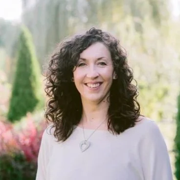 Rebecca Stewart, RMT, smiling outdoors in a park or garden setting.