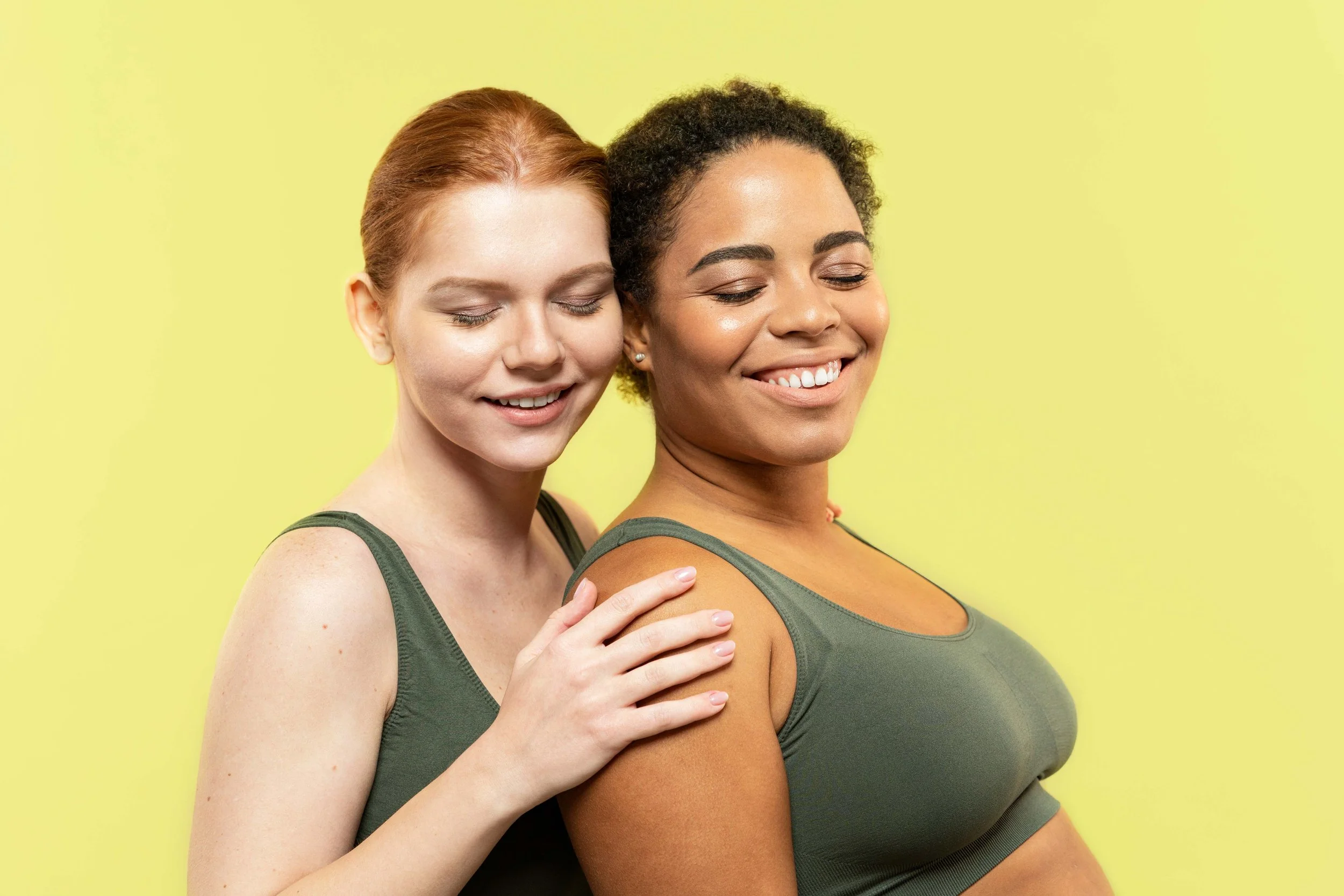 Two women smiling - woman with red hair is hugging woman with black hair from behind