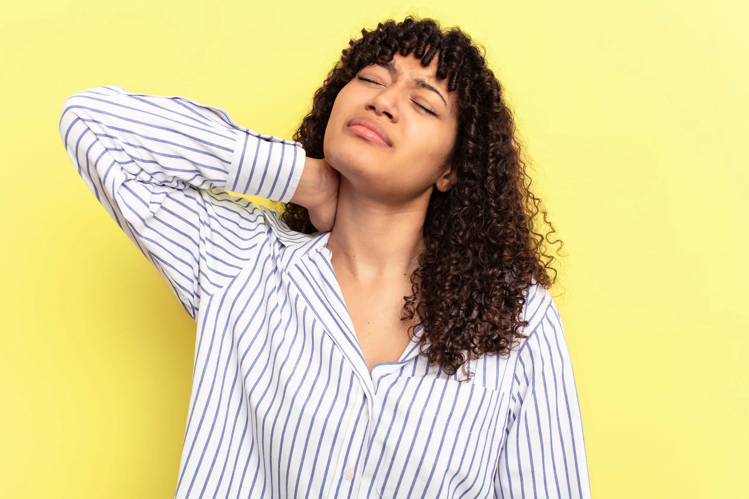 Woman in pain holding her neck, against a yellow background