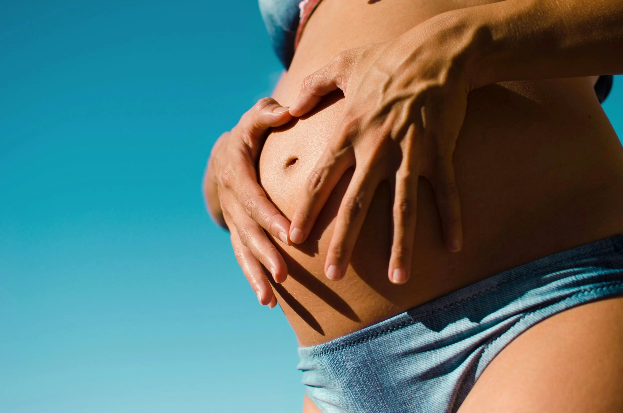 Pregnant woman holding belly against blue sky