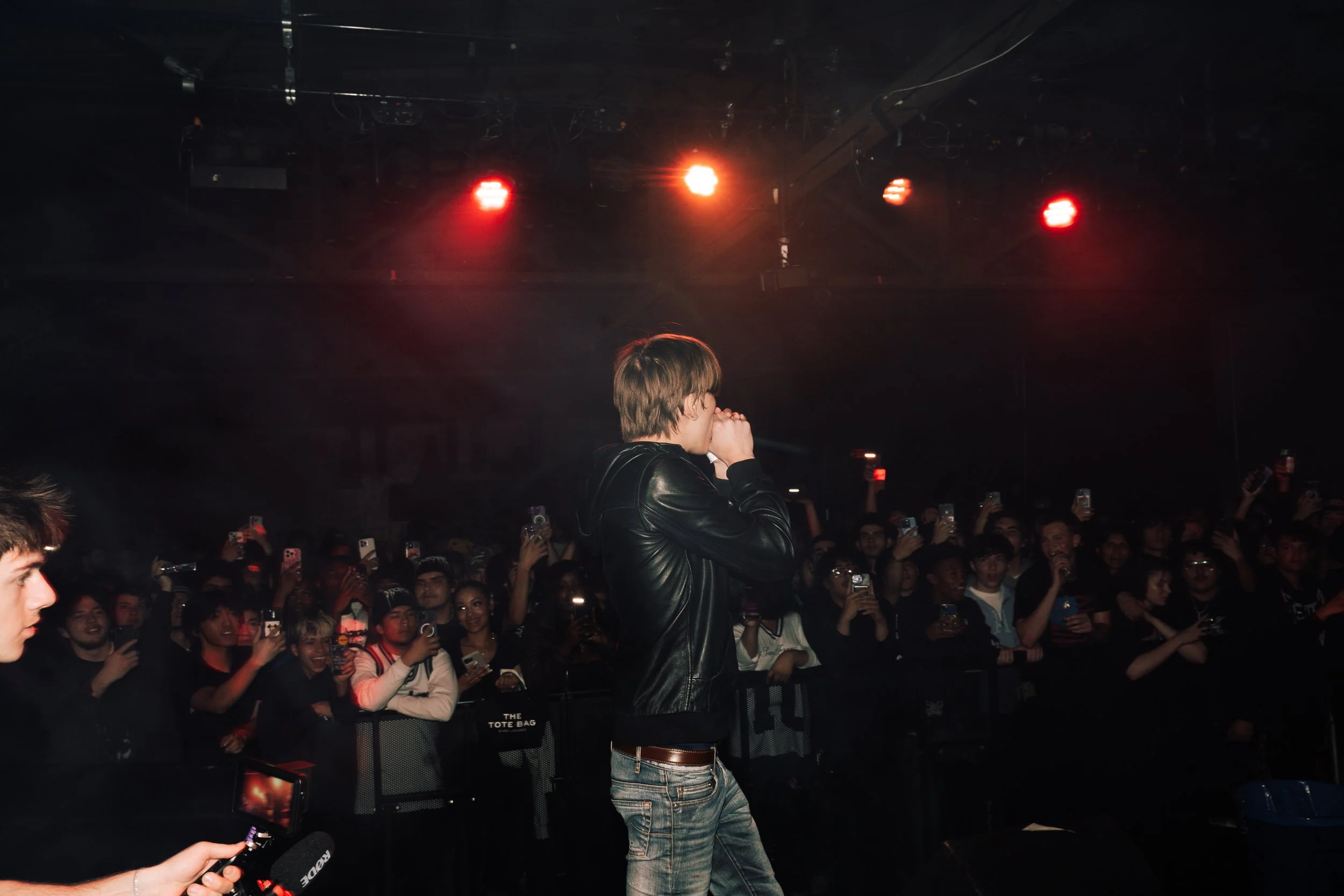 A male performer singing into a microphone on stage with a crowd watching at a concert.