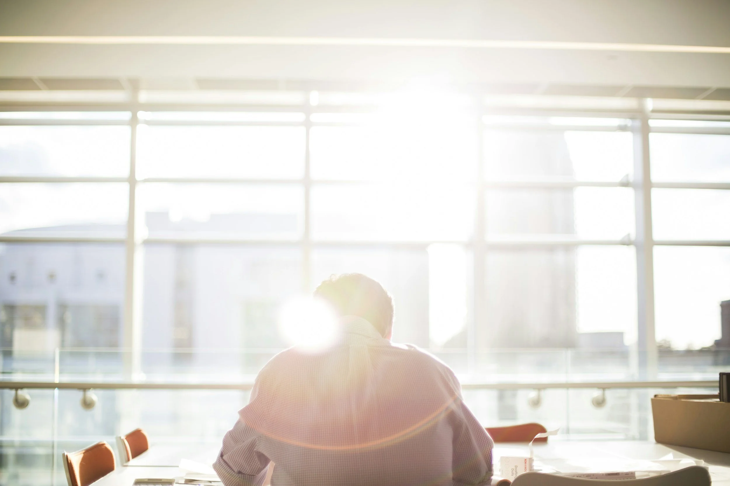 Person sitting at a desk in a bright room with large windows and sunlight streaming in.