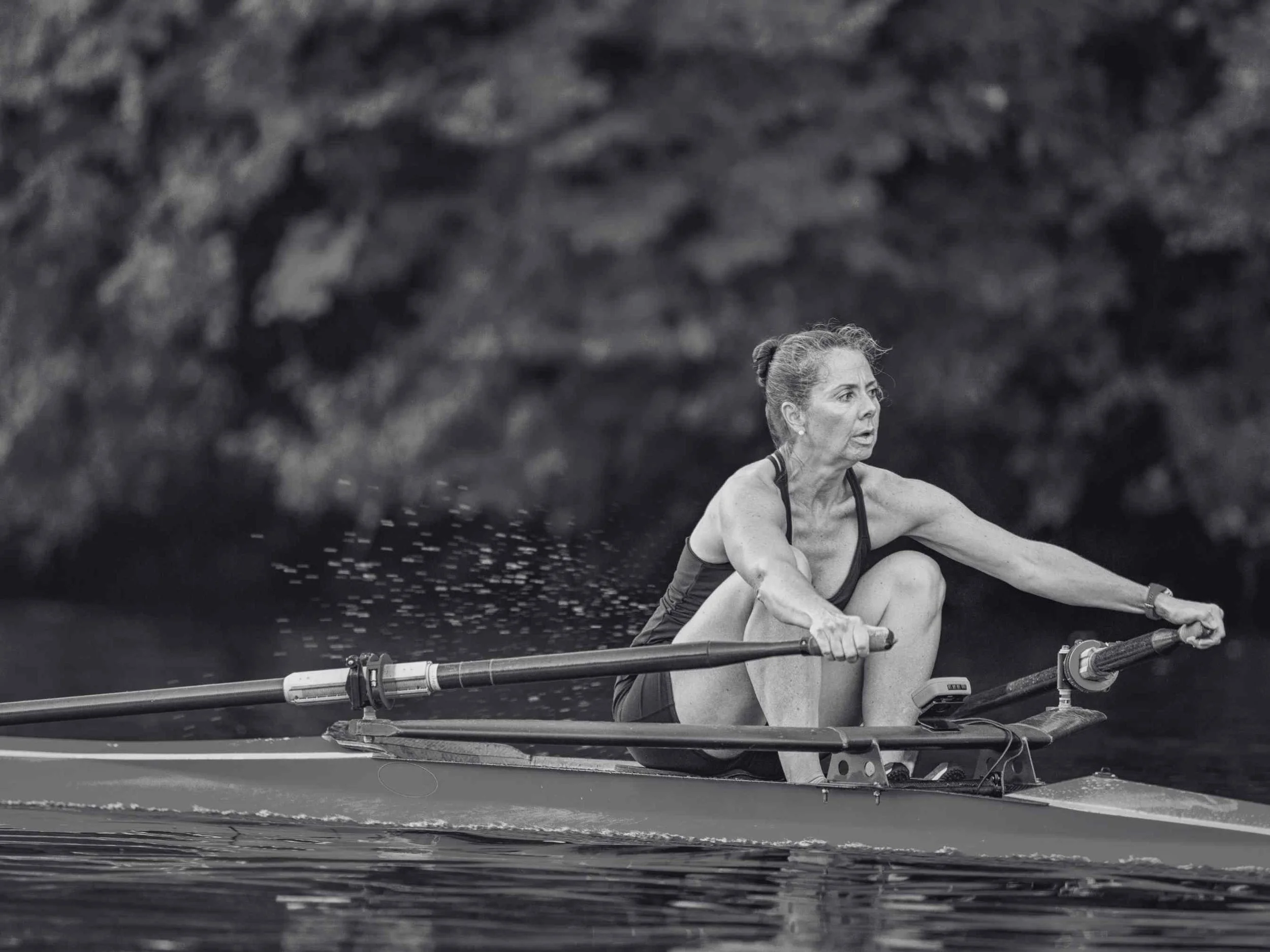 A woman rowing a boat on a body of water with a rocky background, wearing a tank top and shorts.