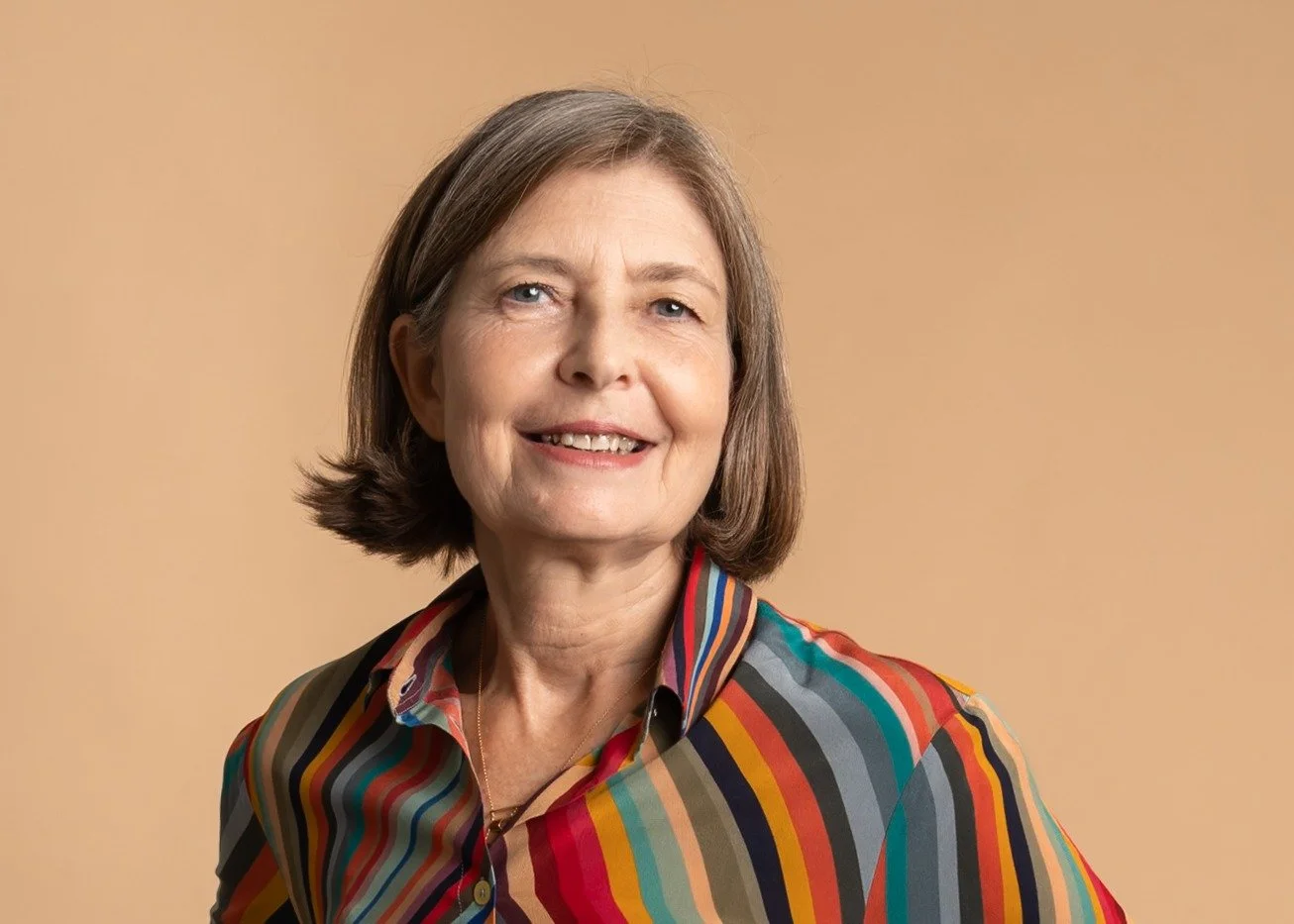 Flore Cassin executive and entreprenur coach smiling wearing a colourful striped shirt against a beige background.