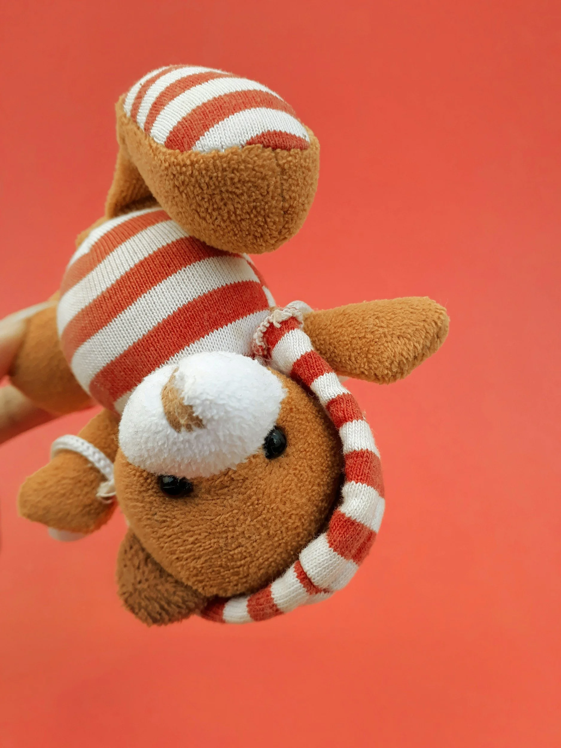 A plush toy of a horse wearing a red and white striped hat, with a white tuft on its head, set against a pink background.