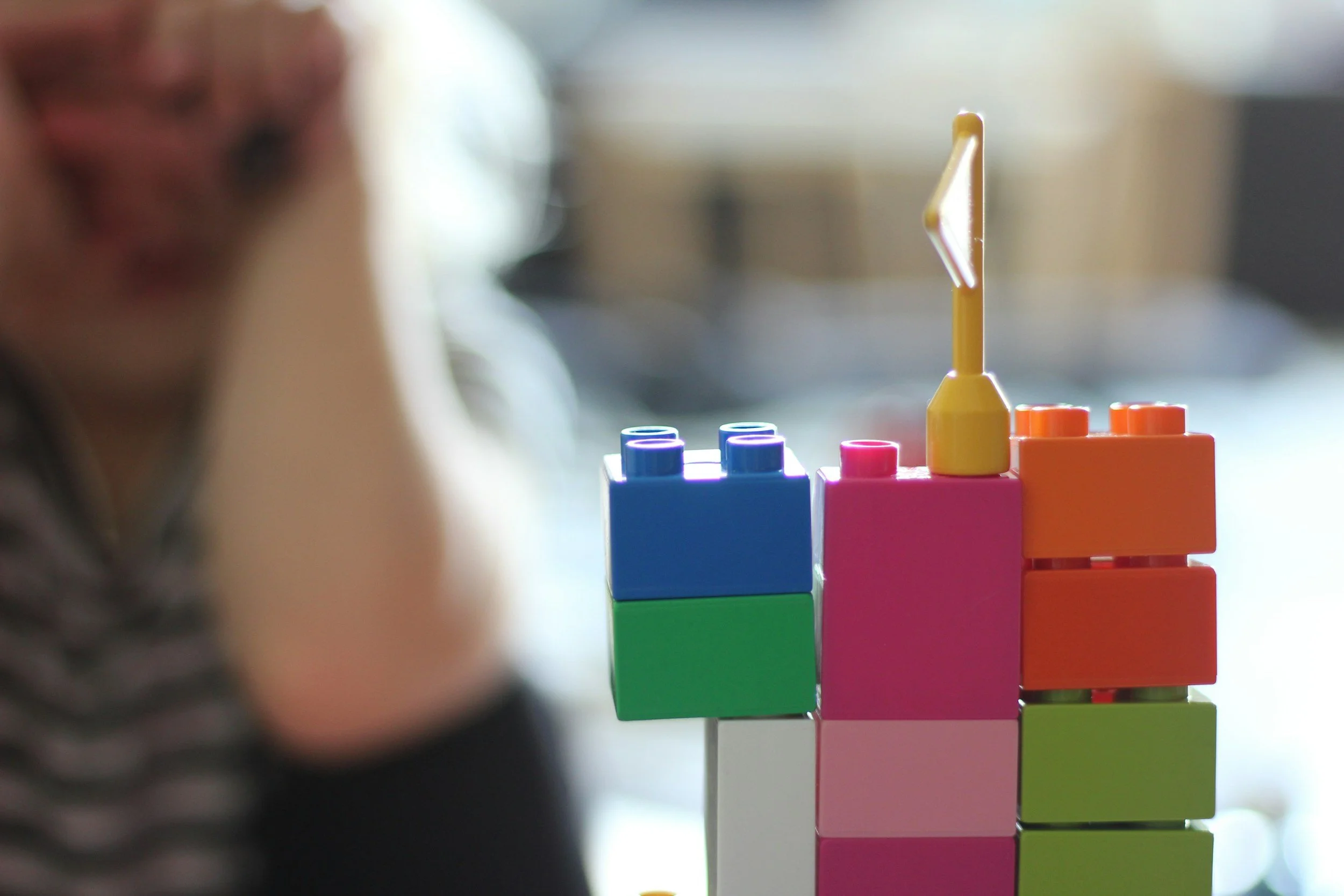 Close-up of colorful plastic building blocks stacked on each other with a person blurred in the background.