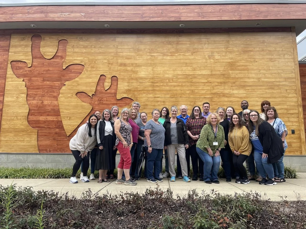 Group Photo of the Greater Nashville Chapter at the Nashville Zoo. They are posing next to a wall that depicts the outlines of giraffes.