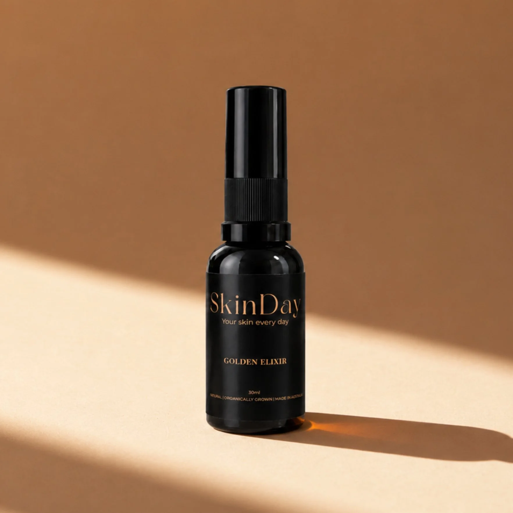 A black spray bottle labeled 'SkinDay Golden Elixir' standing on a beige surface with a brown background.