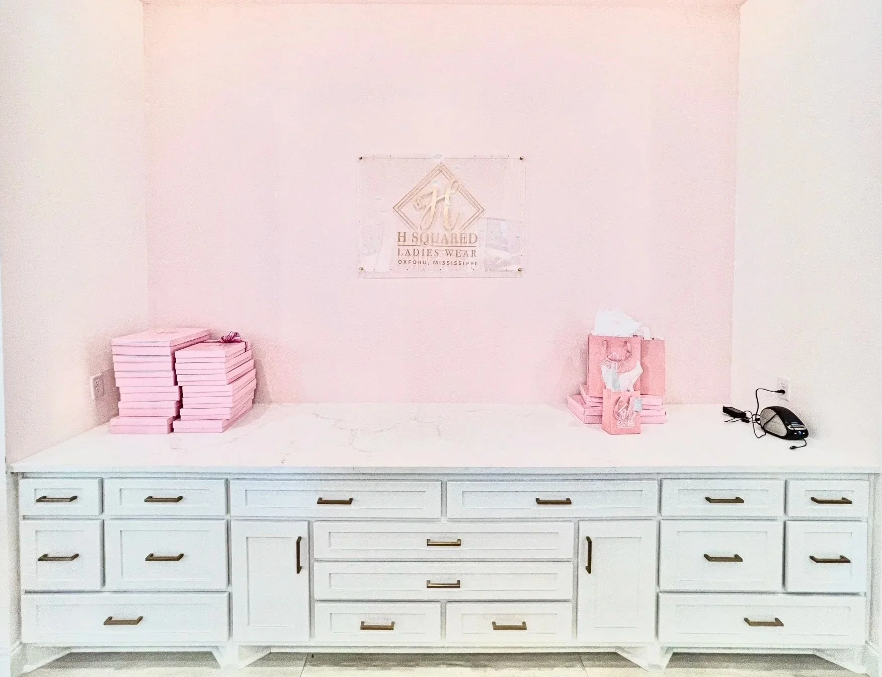 White cabinet with multiple drawers against a pink wall, with pink boxes on either side and a laboratory phone on the right.