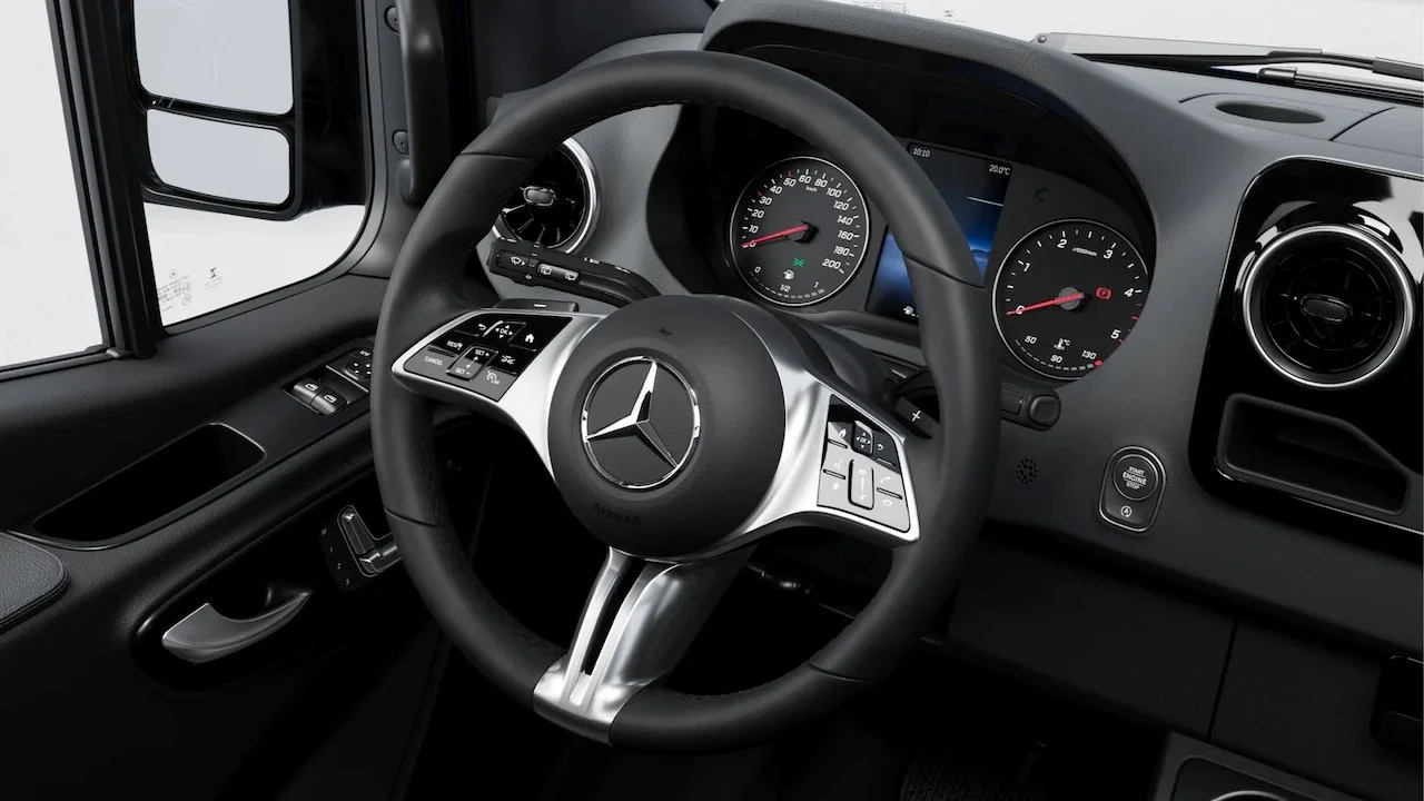 Interior of a Mercedes-Benz vehicle showing the steering wheel with the Mercedes logo, dashboard, and instrument cluster.