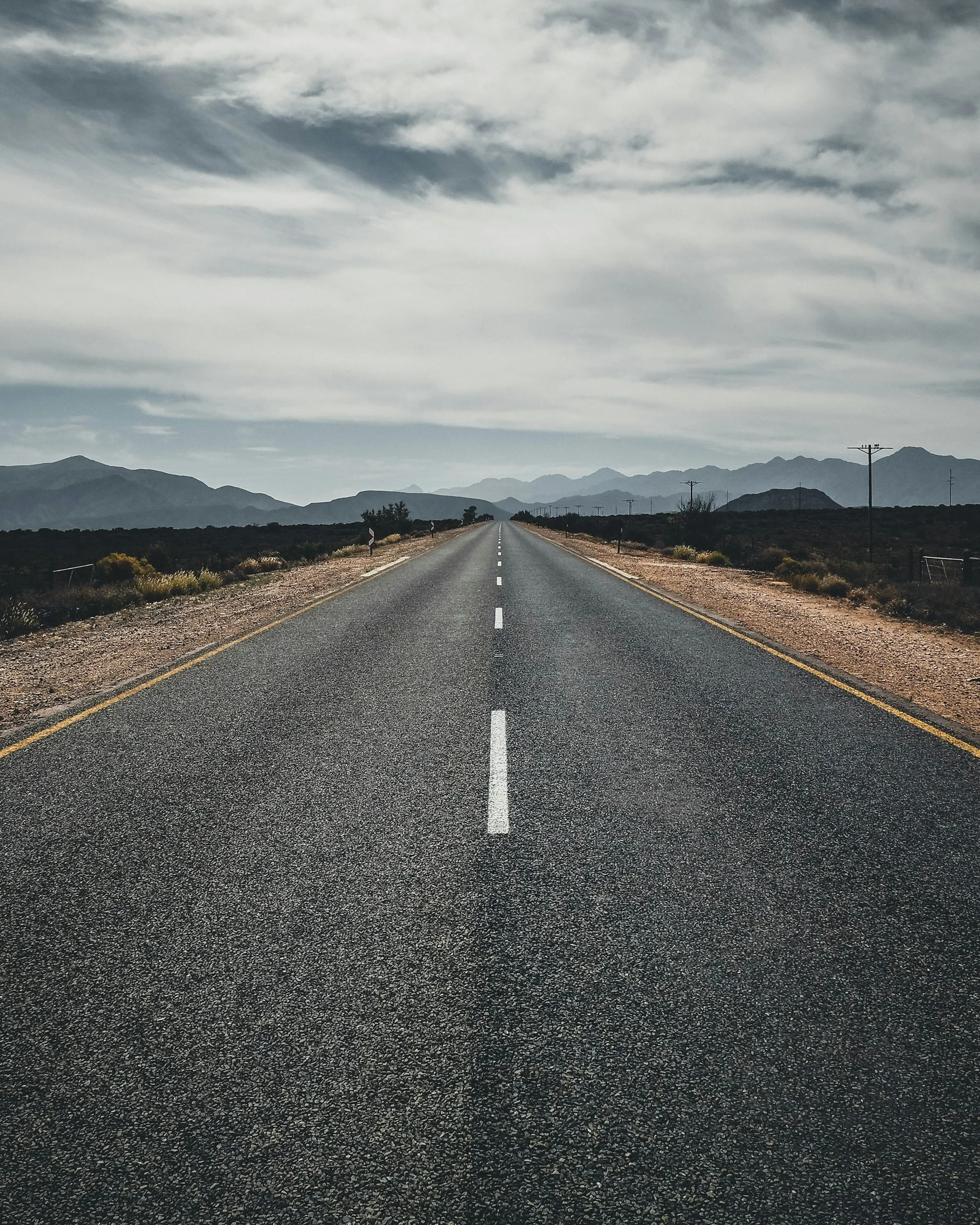 Empty road extending towards distant mountains under partly cloudy sky.