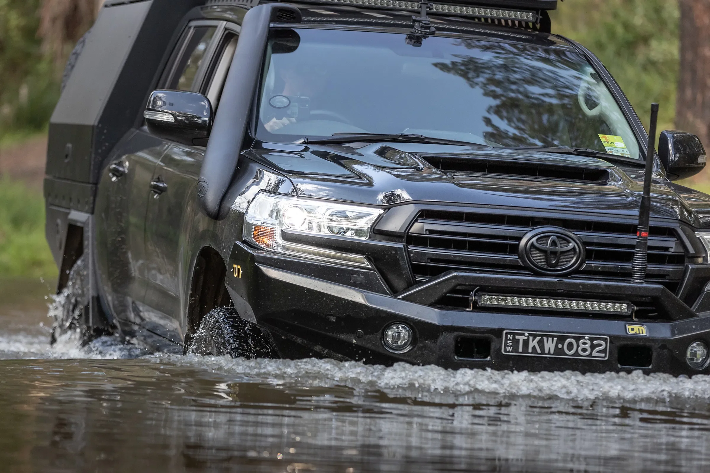 A black Toyota Land Cruiser driving through a shallow water crossing outdoors.