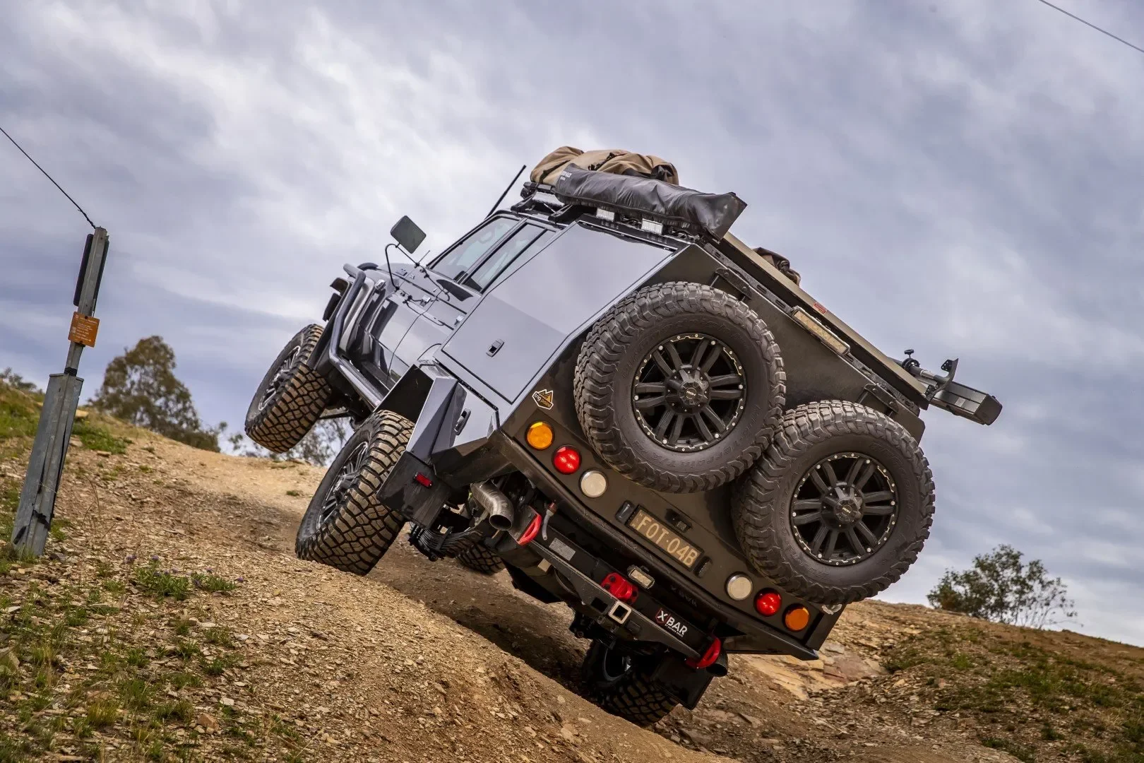 A black off-road vehicle navigating a steep dirt incline on a cloudy day.