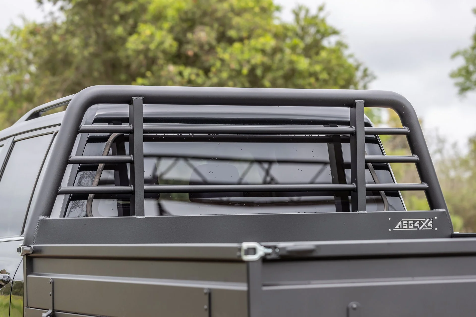 Close-up of the back of a gray utility vehicle with a protective roll cage and a rear storage area, outdoors with trees in the background.