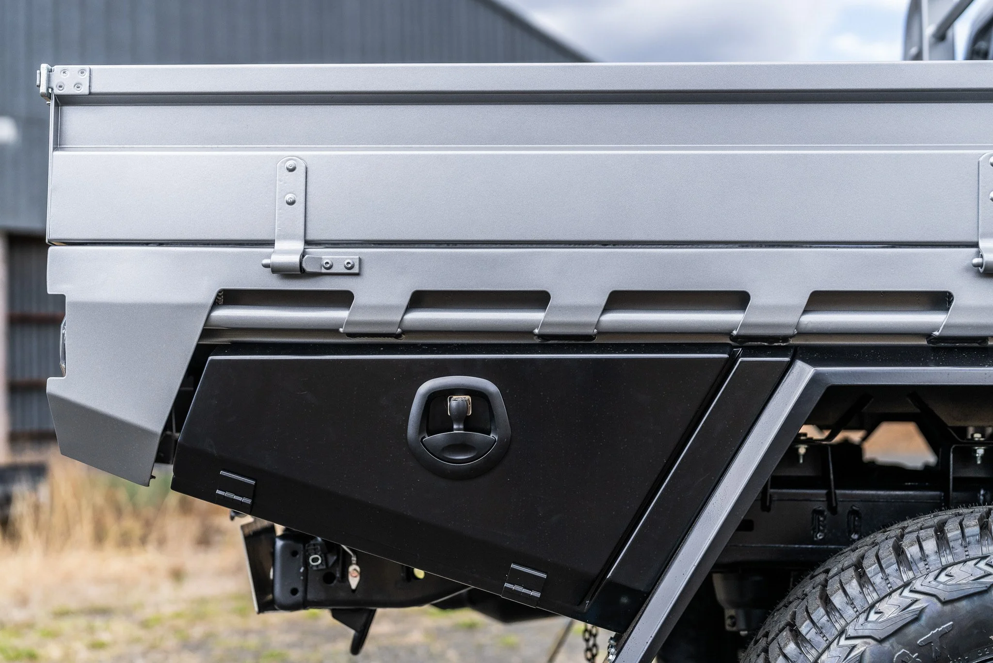 Close-up of the side of a gray utility truck with a black storage box and tire.