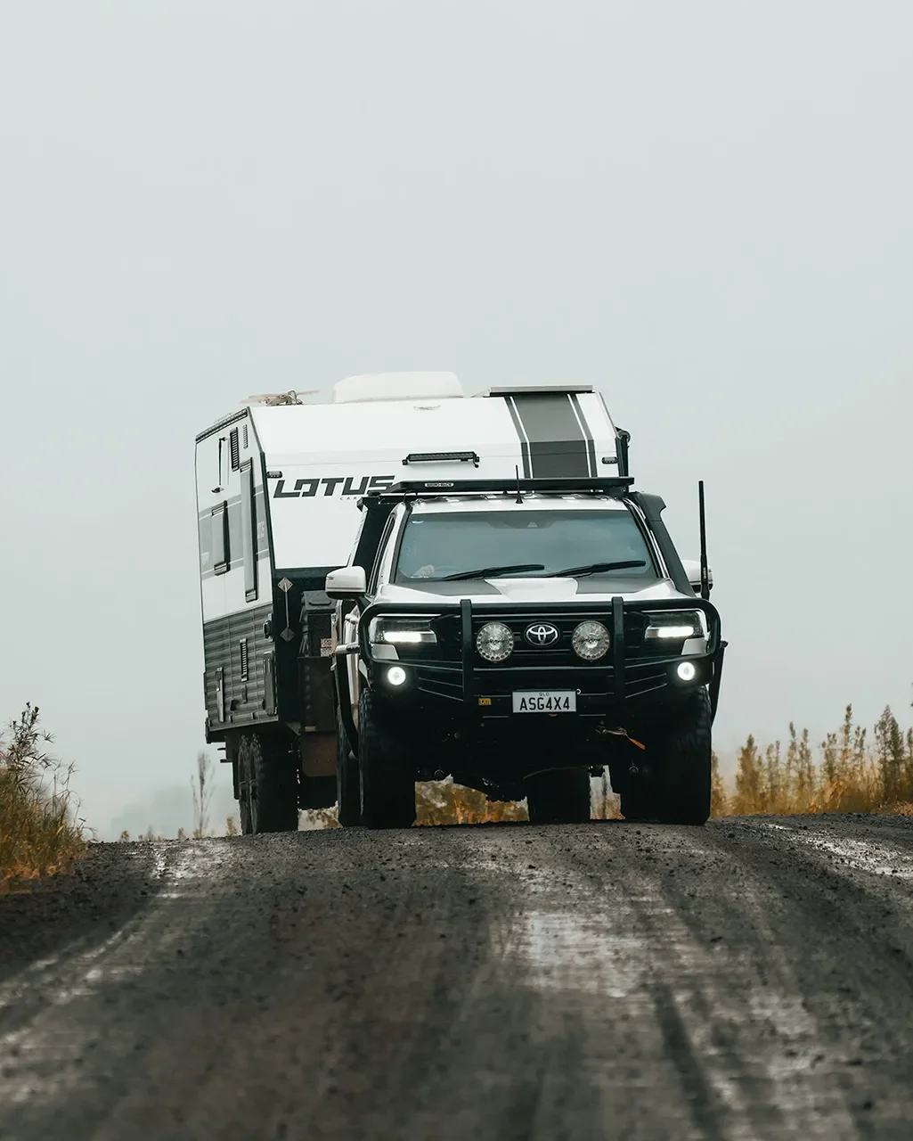Off-road vehicle towing a small camper trailer on a dirt road.