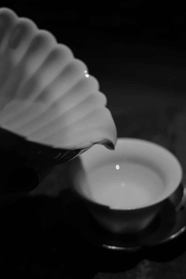 A black-and-white photo of tea being poured from a shell-shaped teapot into a small teacup.