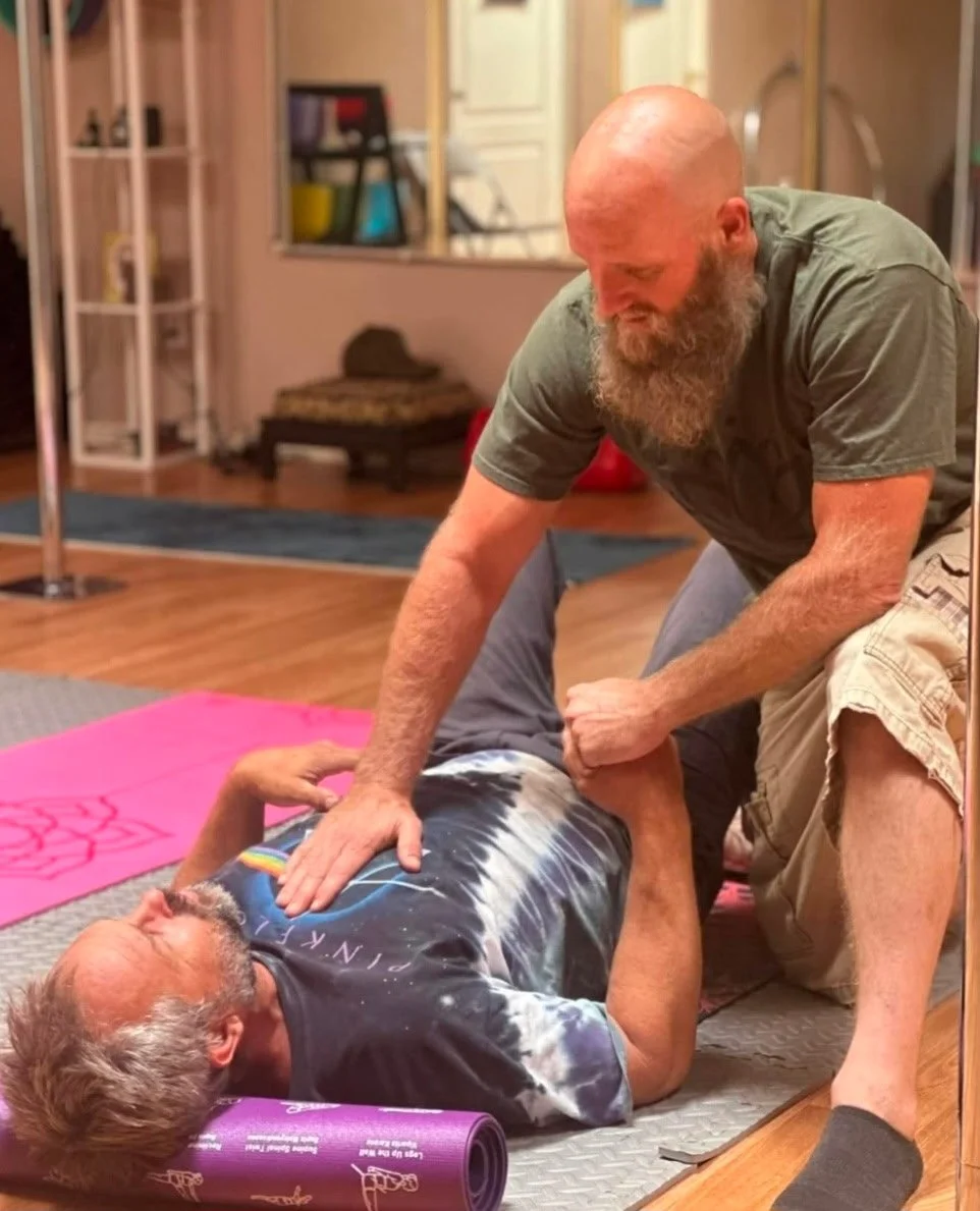 A man performing chest compressions on an elderly man lying on a yoga mat, practicing CPR in a room with wooden floors and background equipment.