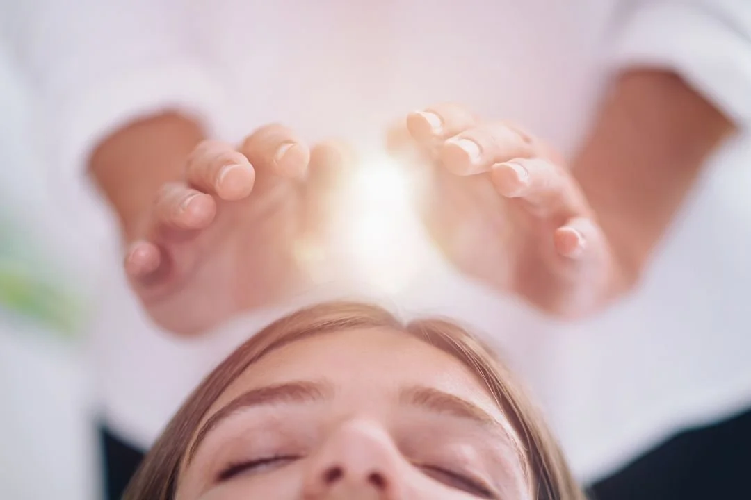 Person with closed eyes receiving a healing energy or light from another person's hands above their forehead.